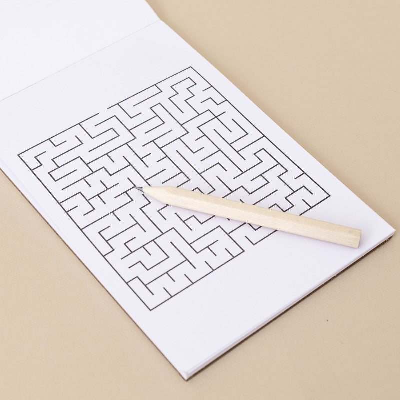 A white puzzle booklet or activity sheet with a black line maze printed on it, placed on a beige surface with a light wooden pencil resting diagonally across the page.