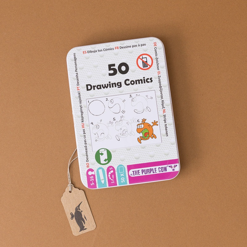 A rectangular metal tin labeled '50 Drawing Comics' with a small hanging paper tag, photographed on a plain warm brown background.