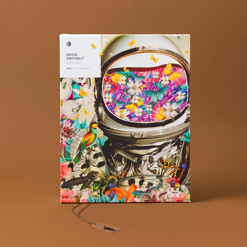 The puzzle 'David Arovbit: The Universe' by David Arovbit is displayed upright on a solid brown background. The cover features a highly detailed, colorful illustration of an astronaut's helmet filled with flowers, surrounded by butterflies, birds, and other nature motifs.