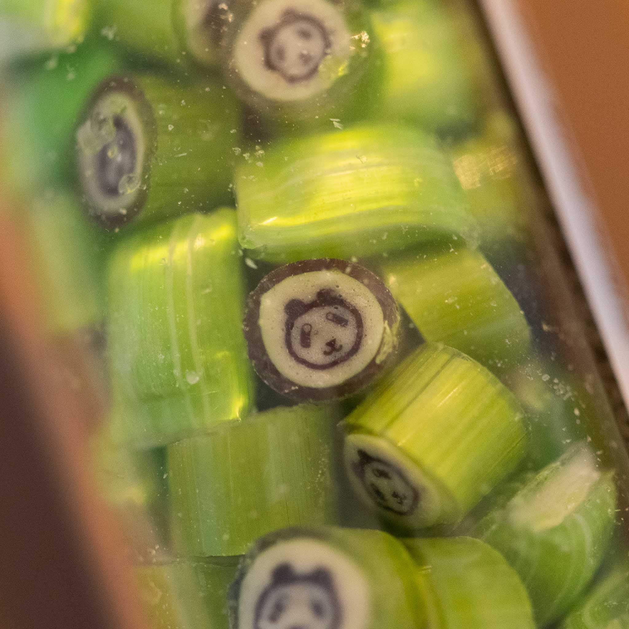 artisanal-hard-candy-tube-guava-panda Green cylindrical candies with panda face design in a clear container.
