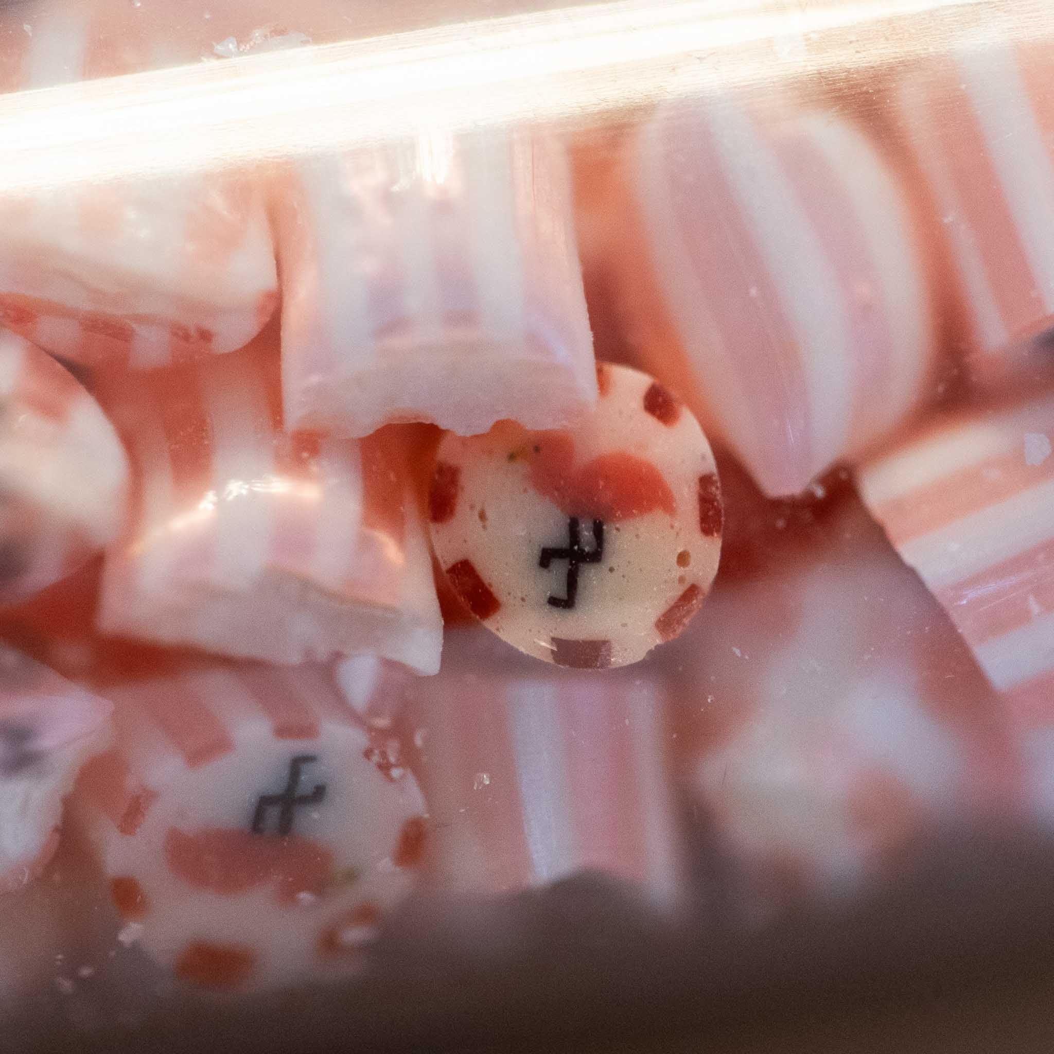 artisanal-hard-candy-tube-strawberry-lemonade-flamingo Close-up of pink and white striped candies with a black symbol on a clear background