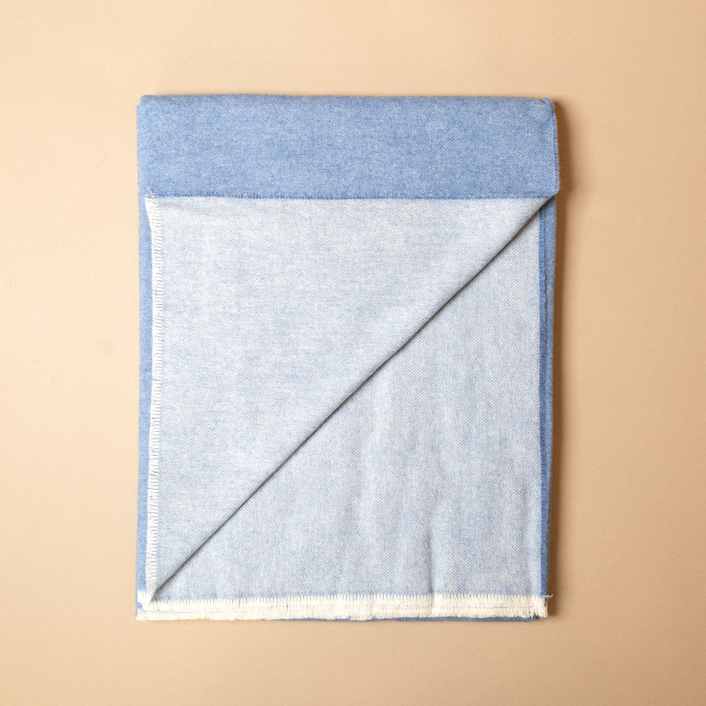 aspen-throw-niagra Folded blue fabric on a beige background