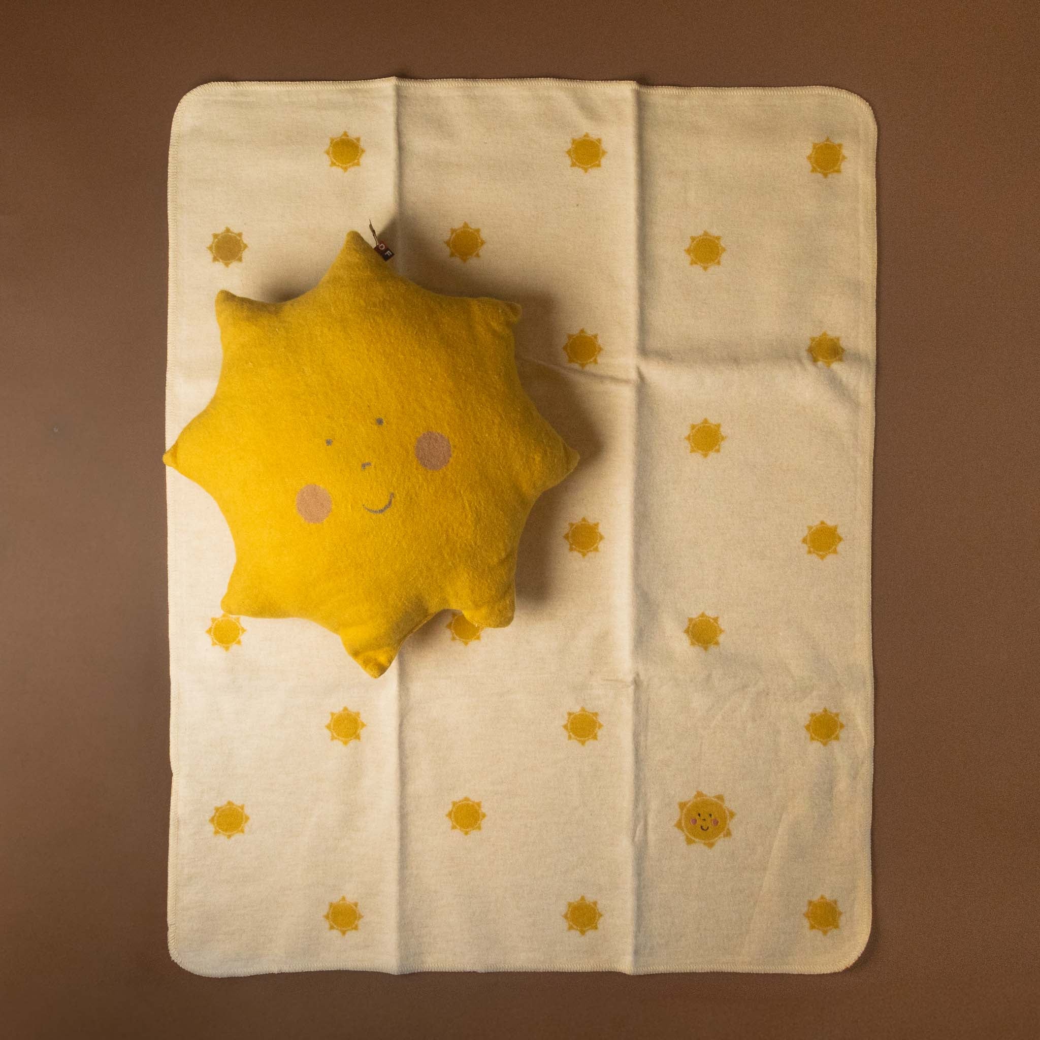 Yellow sun-shaped pillow on a beige blanket with star patterns against a brown background