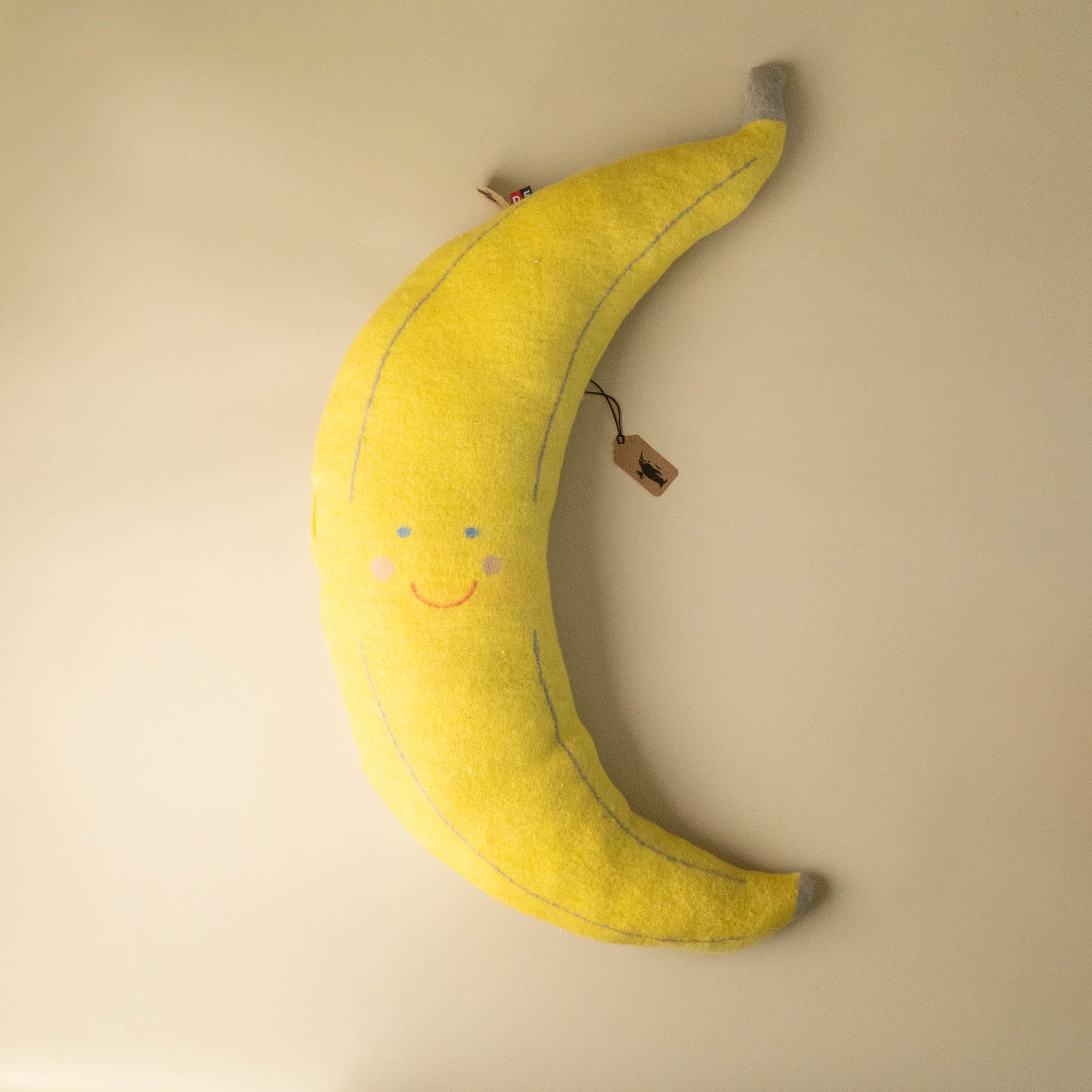 Yellow banana-shaped bananarama-cushion with a smiley face on a beige background