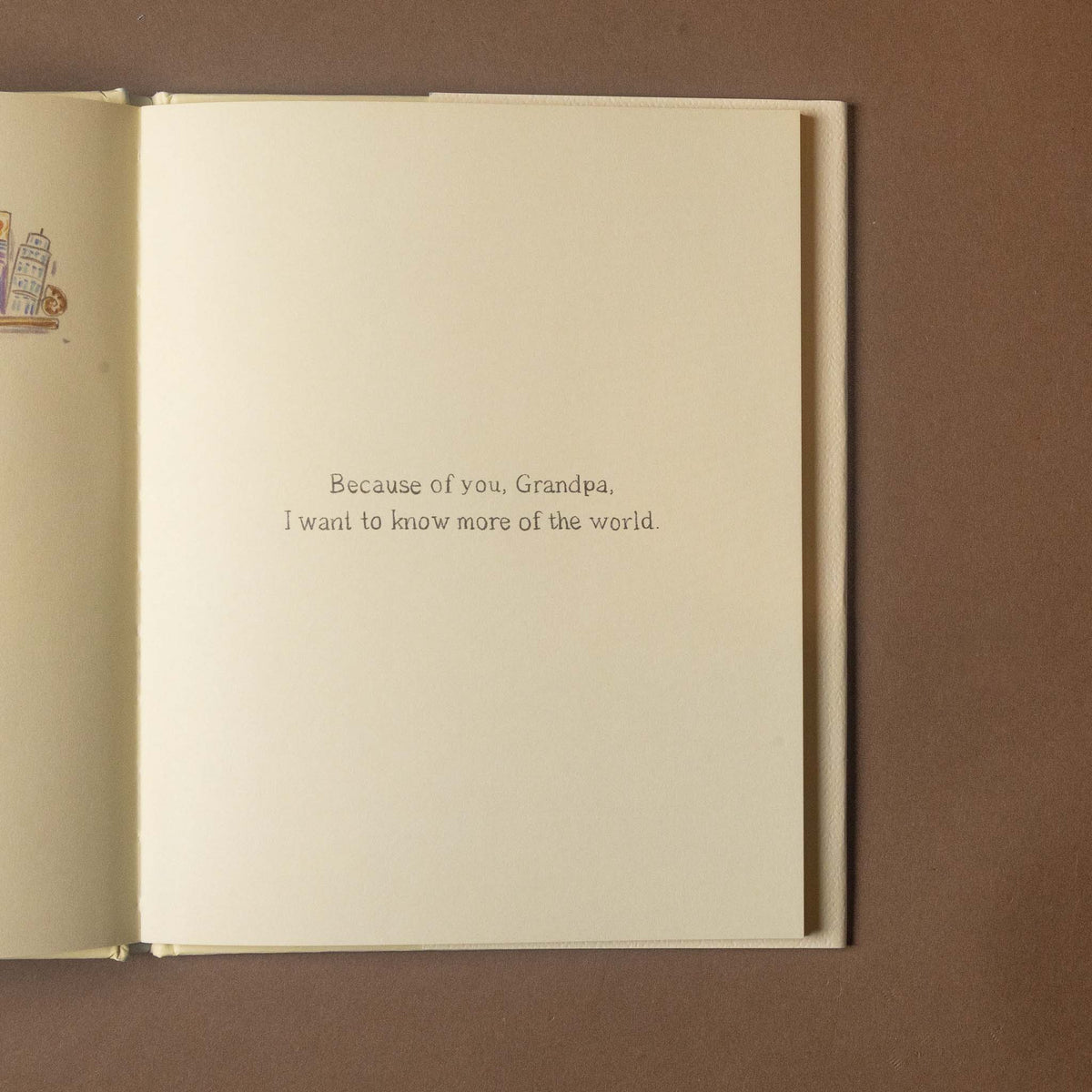 An open book or card with a cream page centered on a brown background, printed with the text: 'Because of you, Grandpa, I want to know more of the world.'.