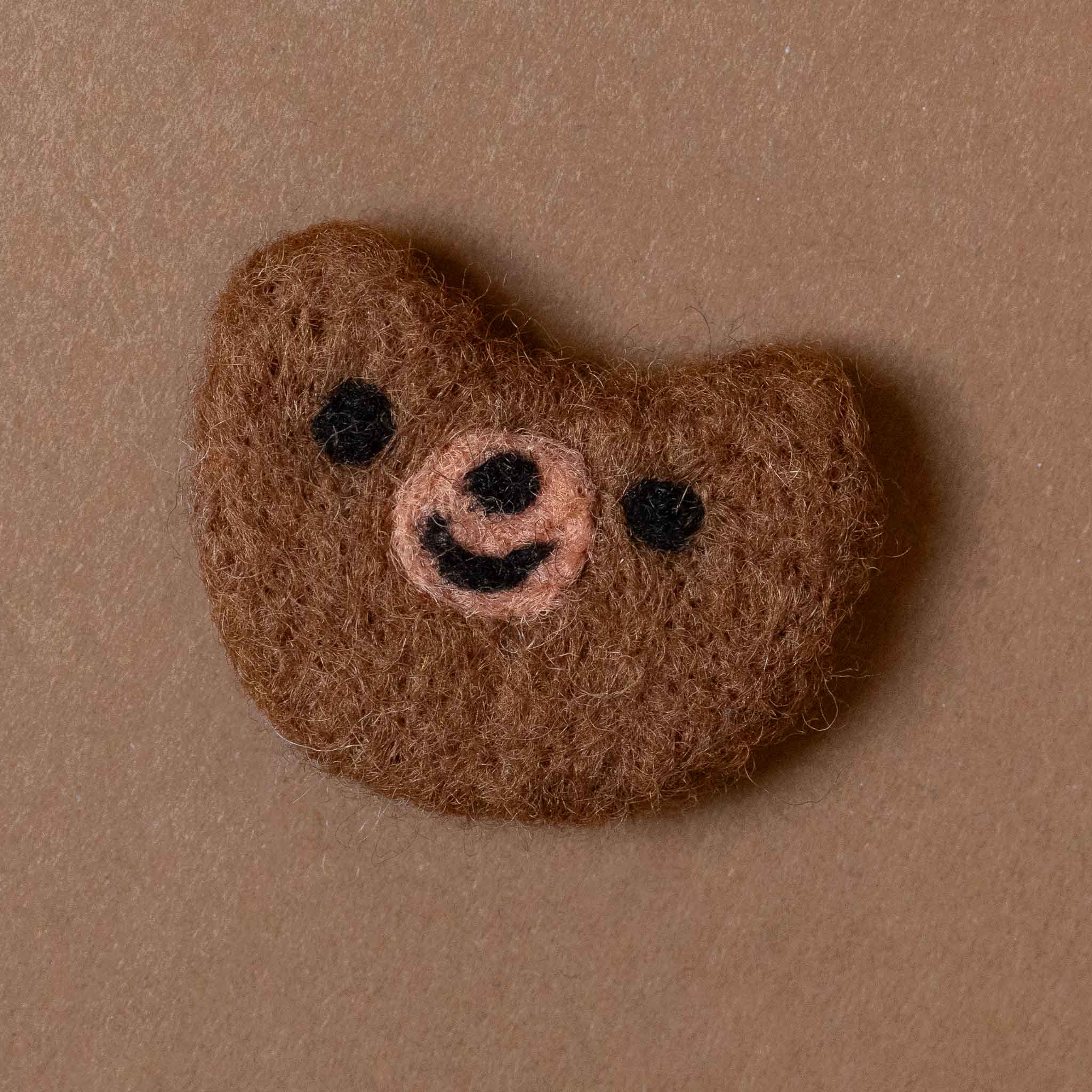 Felted brown bear head on a beige background