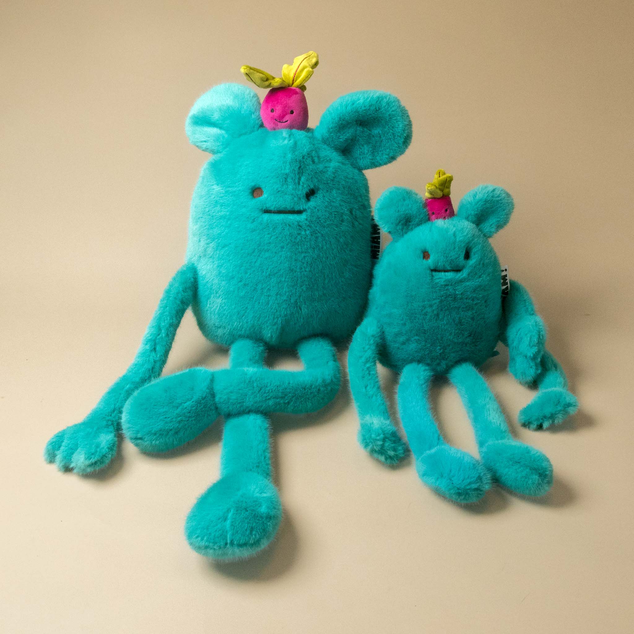 A turquoise blue fuzzy A turquoise blue plush billie-radish-grand and petit toy with long limbs, a small pink flower on its head, and a hangtag, photographed on a plain beige background.plush toy with a small pink and green radish on its head, sitting on a plain beige background.