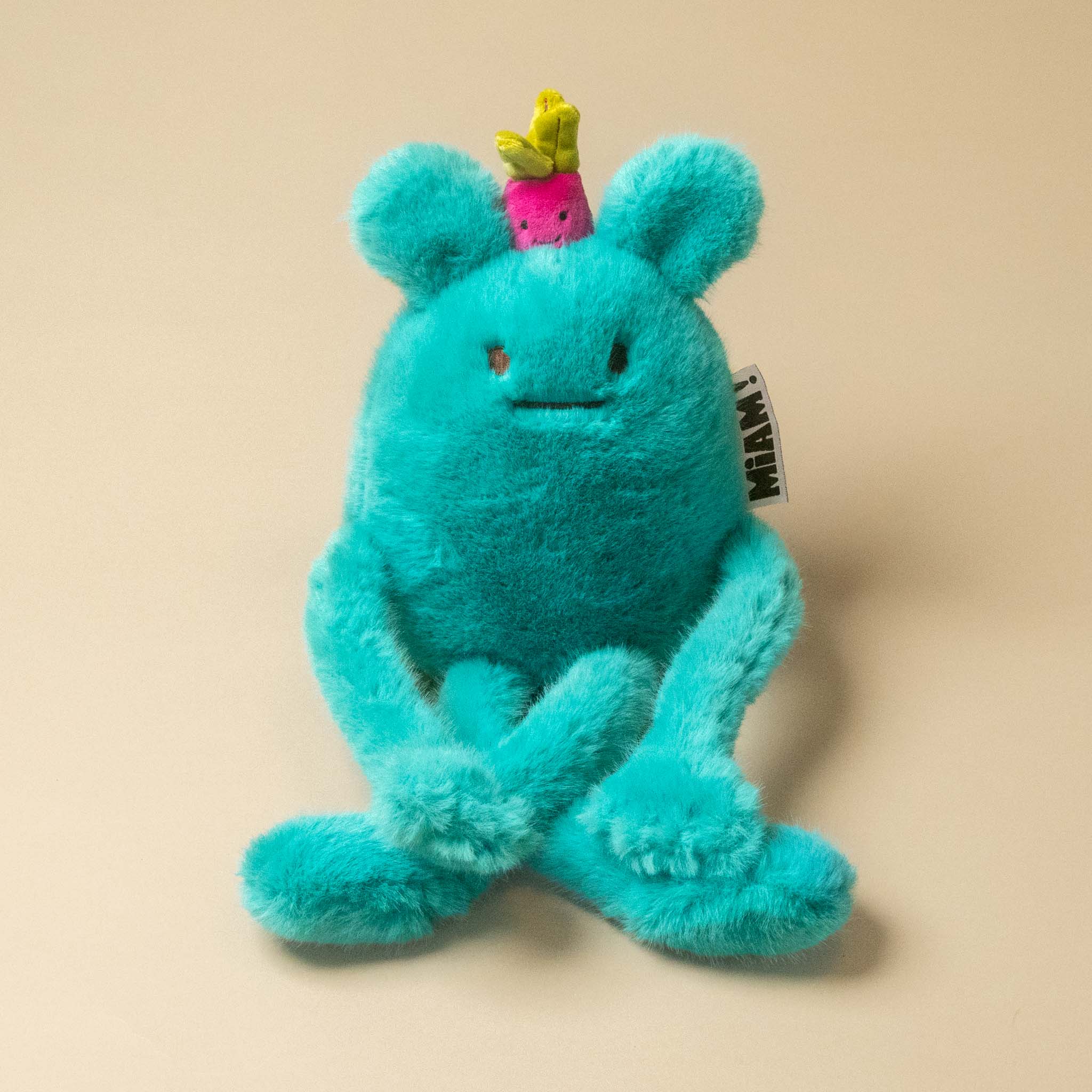 A turquoise blue fuzzy A turquoise blue plush billie-radish-petit toy with long limbs, a small pink flower on its head, and a hangtag, photographed on a plain beige background.plush toy with a small pink and green radish on its head, sitting on a plain beige background.