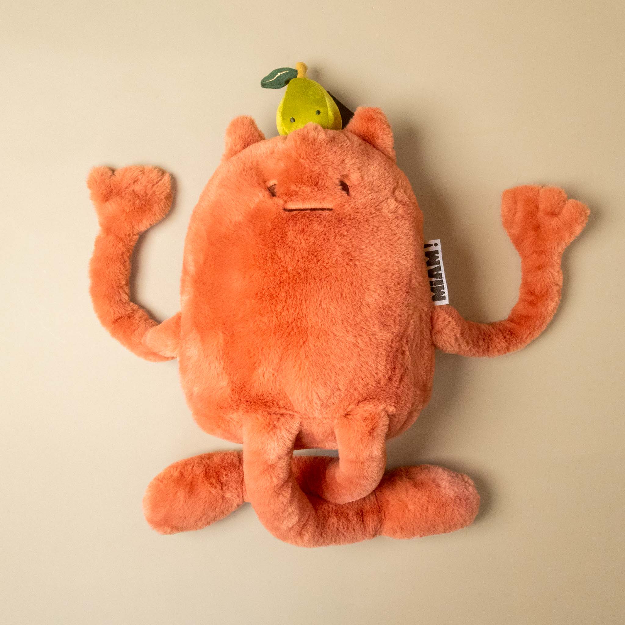 An orange plush britney-pear-grand toy with long limbs and a small yellow pear character on its head, photographed on a plain beige studio background.