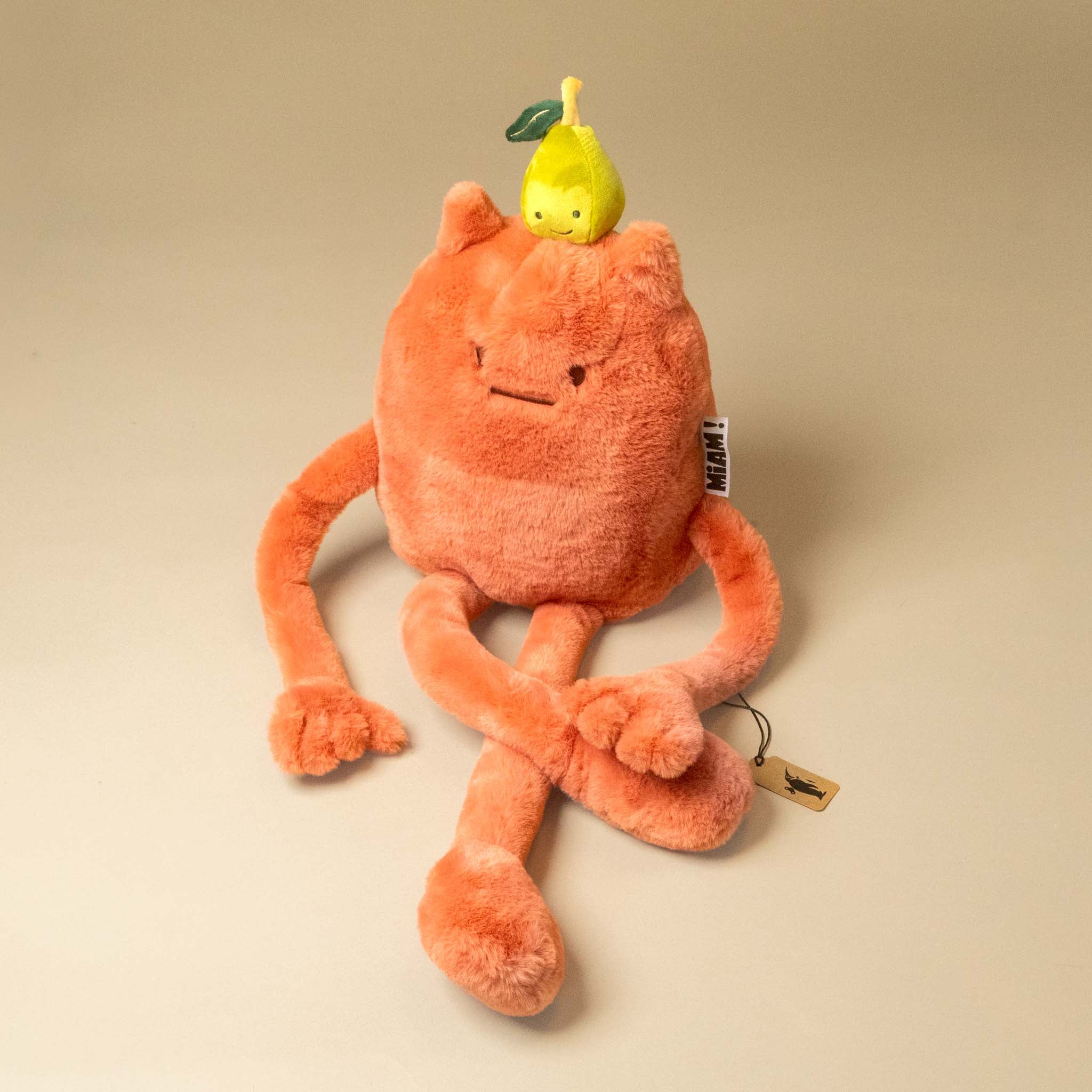 An orange plush britney-pear-grand toy with long limbs and a small yellow pear character on its head, photographed on a plain beige studio background.