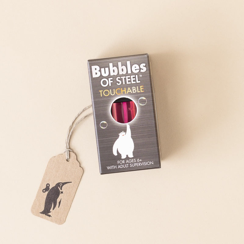 A boxed toy product labeled 'Bubbles of Steel Touchable' with a small hanging kraft paper tag, photographed on a plain warm beige background.