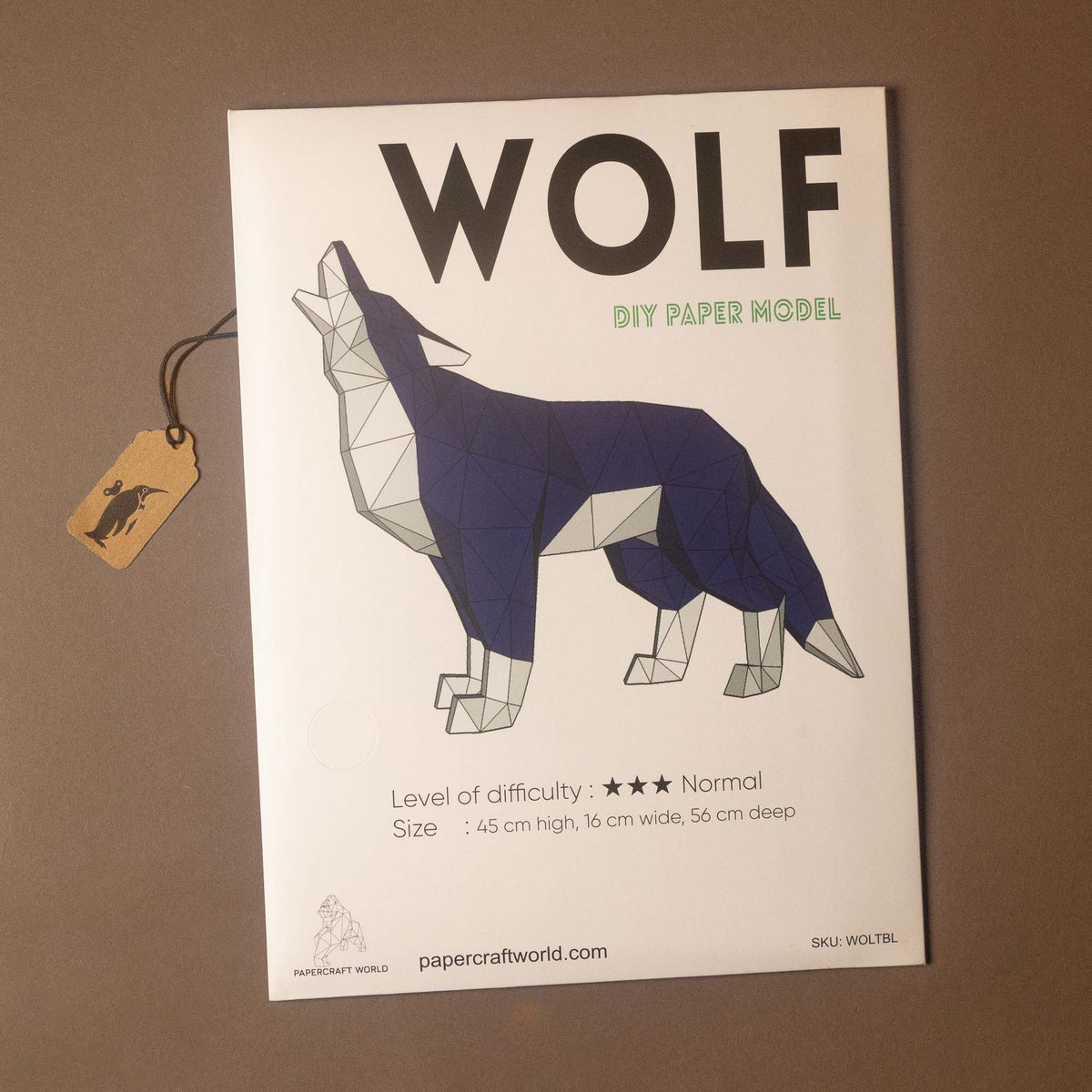 A DIY paper model kit for making a wolf, shown as a white instruction sheet with a geometric wolf illustration, a hanging paper tag, and a brown background.