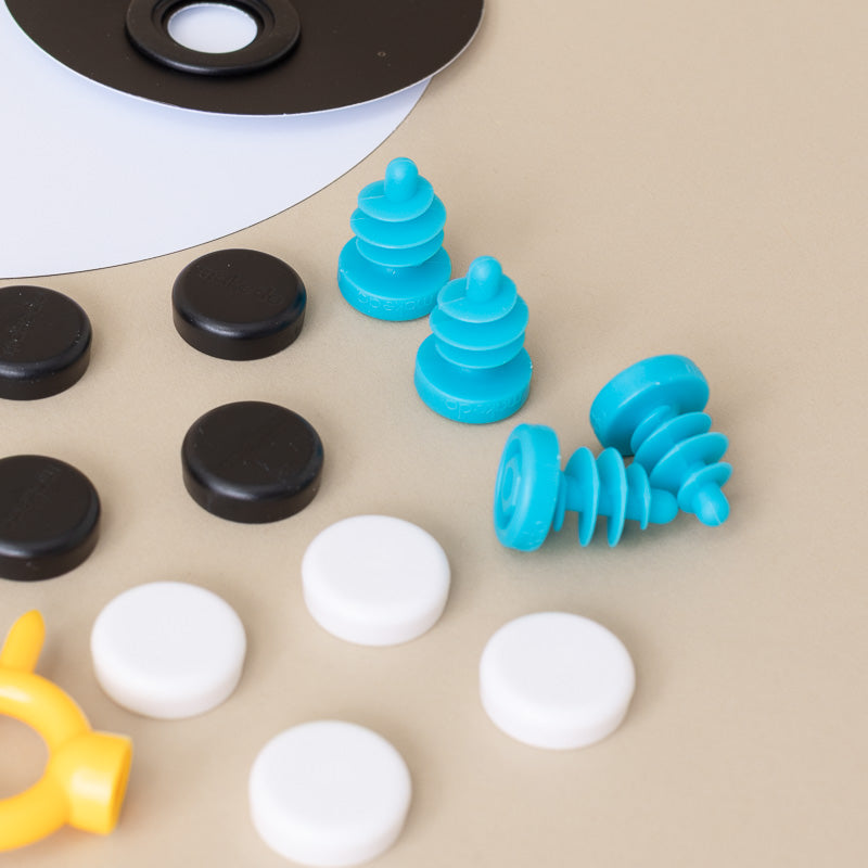 A set of small circular and spiral plastic pieces in black, white, turquoise blue, and yellow arranged on a beige surface, with part of a black-and-white circular component visible at the top.
