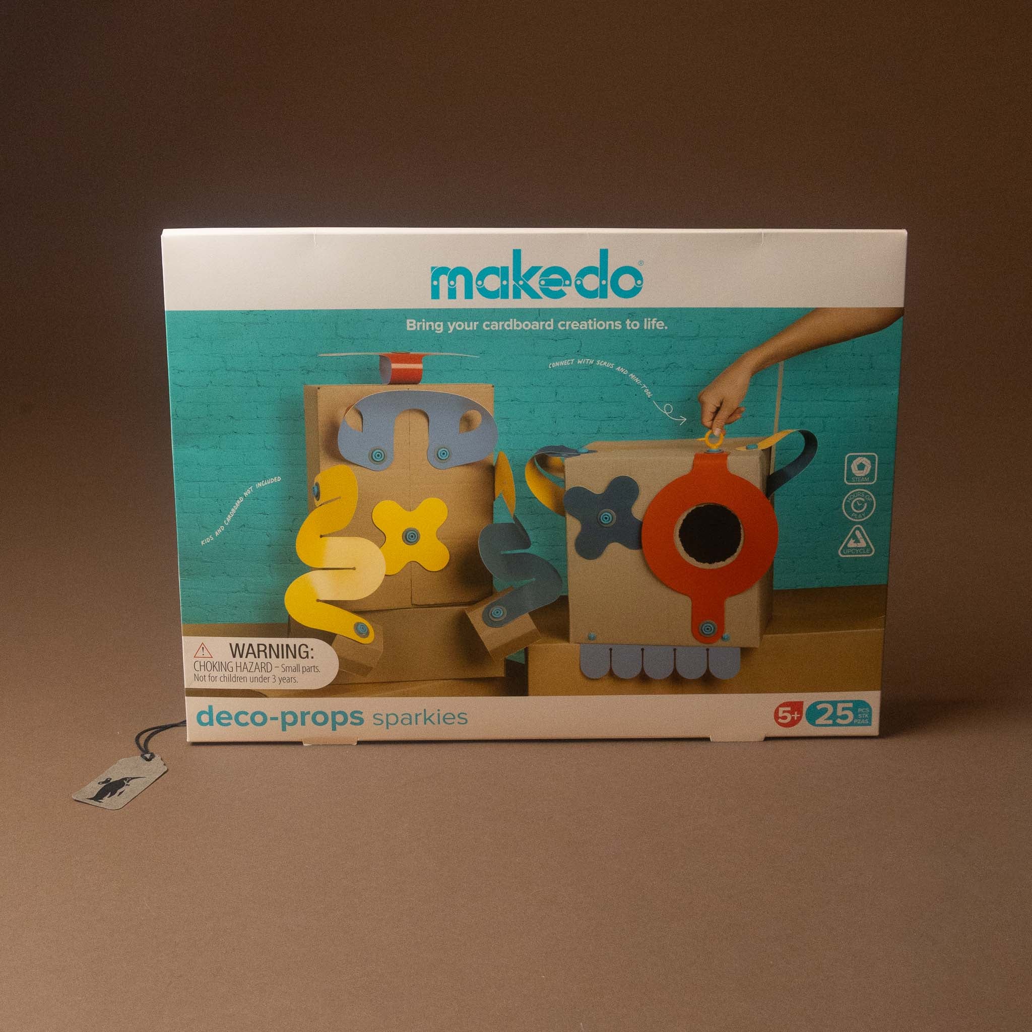 Makedo Deco Props Sparkles toy set in its original retail packaging, displayed on a brown surface against a matching brown background.