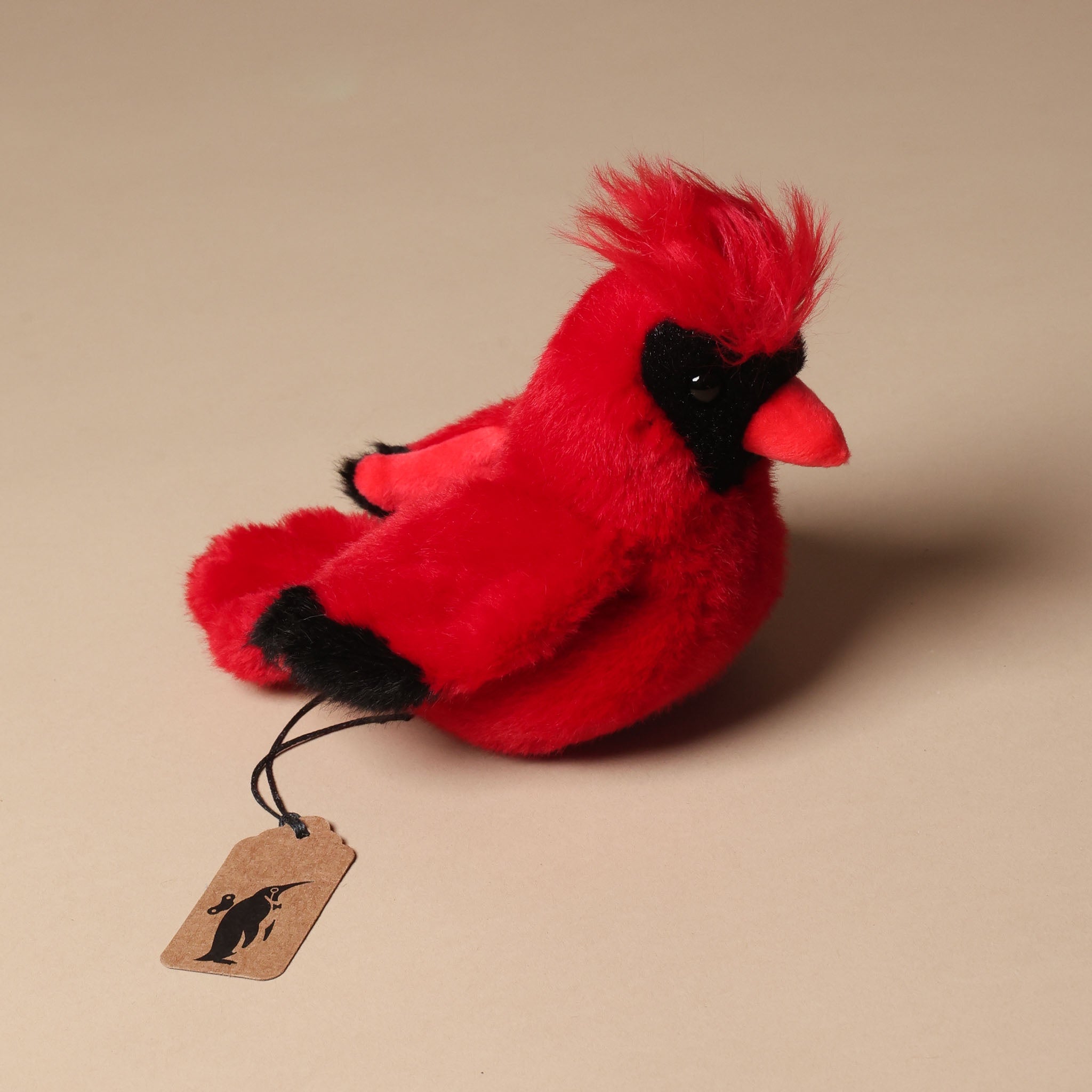 Red plush cardinal bird with a tag on a beige background