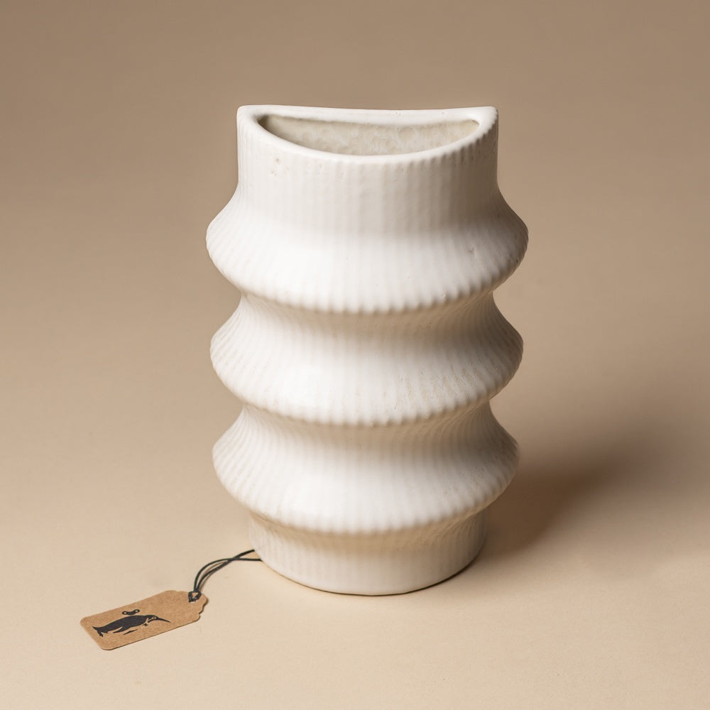 claude-bookend-vase-ripple White textured vase on a beige background with a small tag attached.