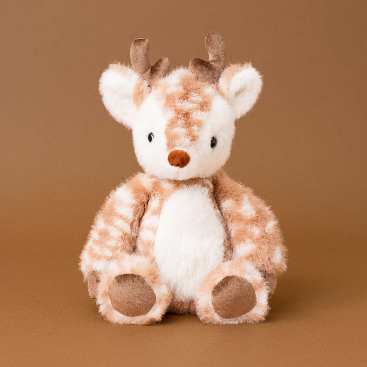 A plush stuffed deer toy with brown and cream fur, small brown antlers, and a soft warm brown background.