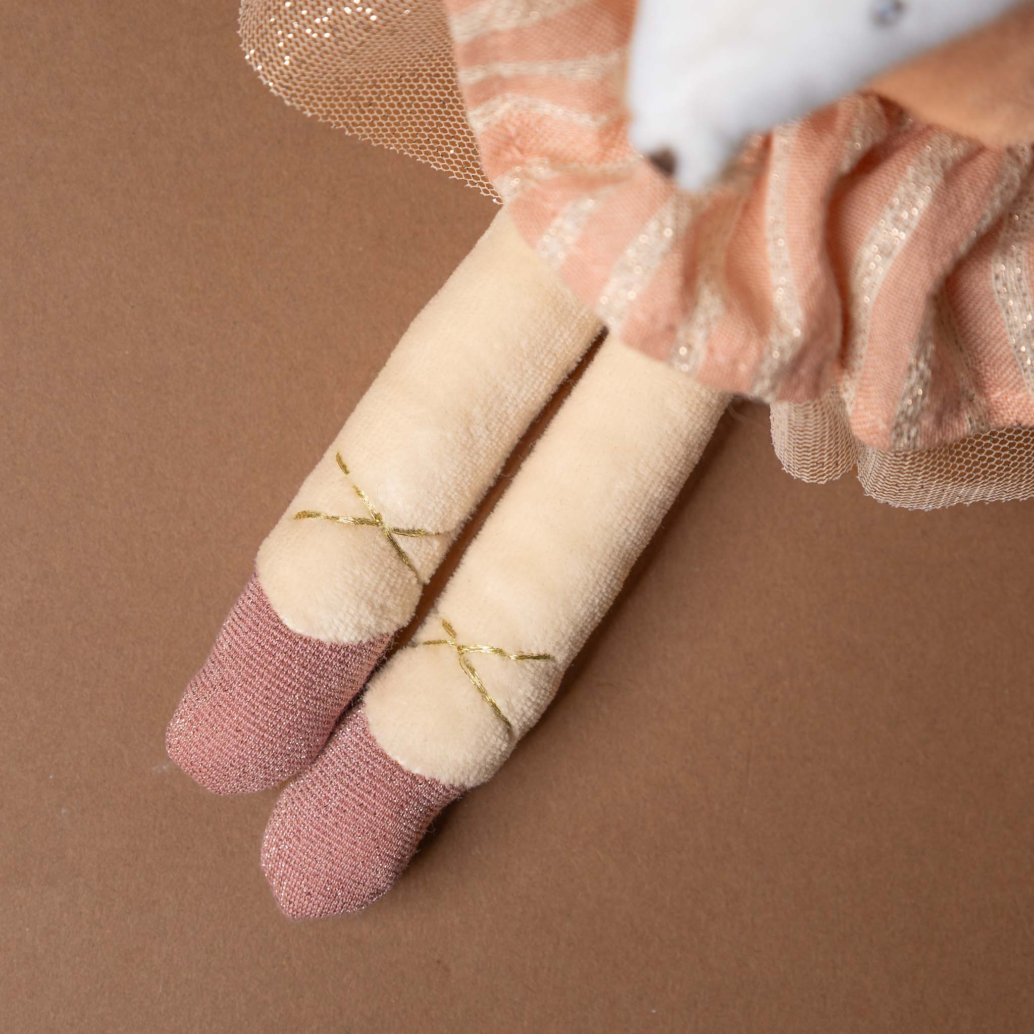 dance-mouse-rose Close-up of a hand wearing pink and gold glittery gloves holding a small beige doll with pink shoes on a brown background.