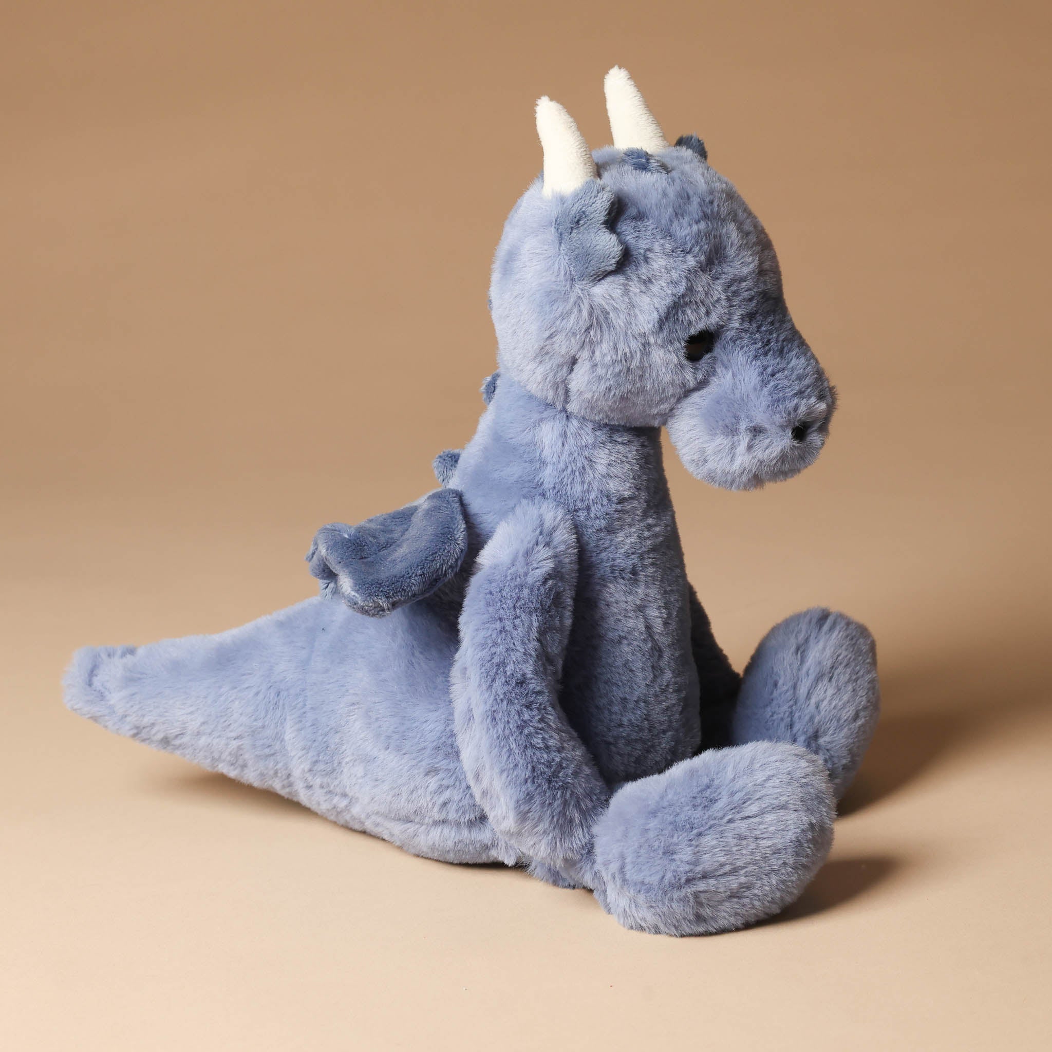 draco-dragon-denim Blue plush toy with white horns on a beige background
