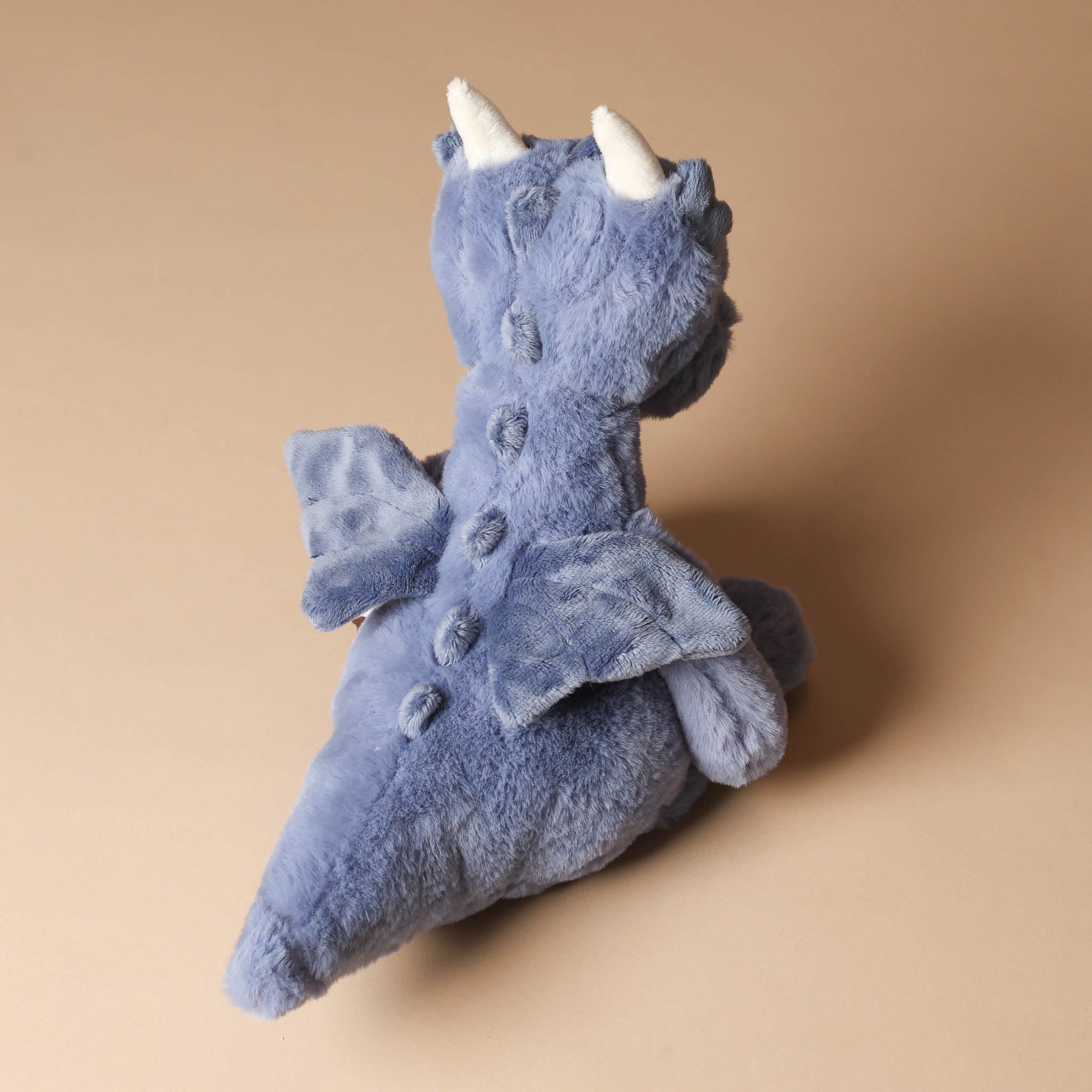 draco-dragon-denim Blue plush toy with white horns on a beige background
