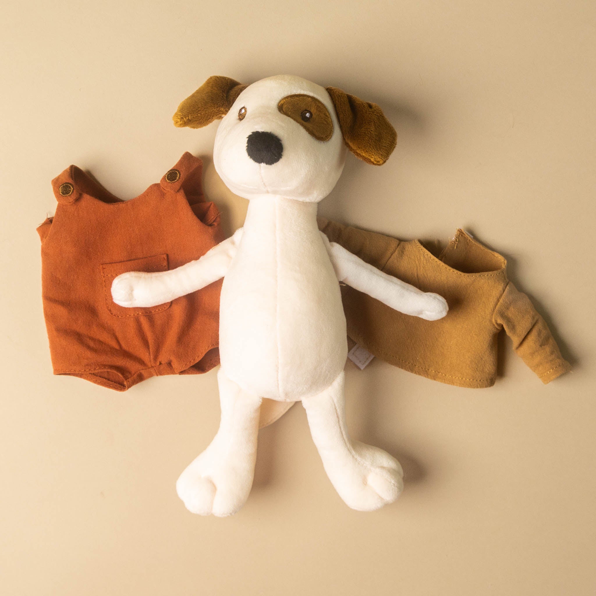 Stuffed eddie-the-pup toy with orange and brown outfits on a beige background