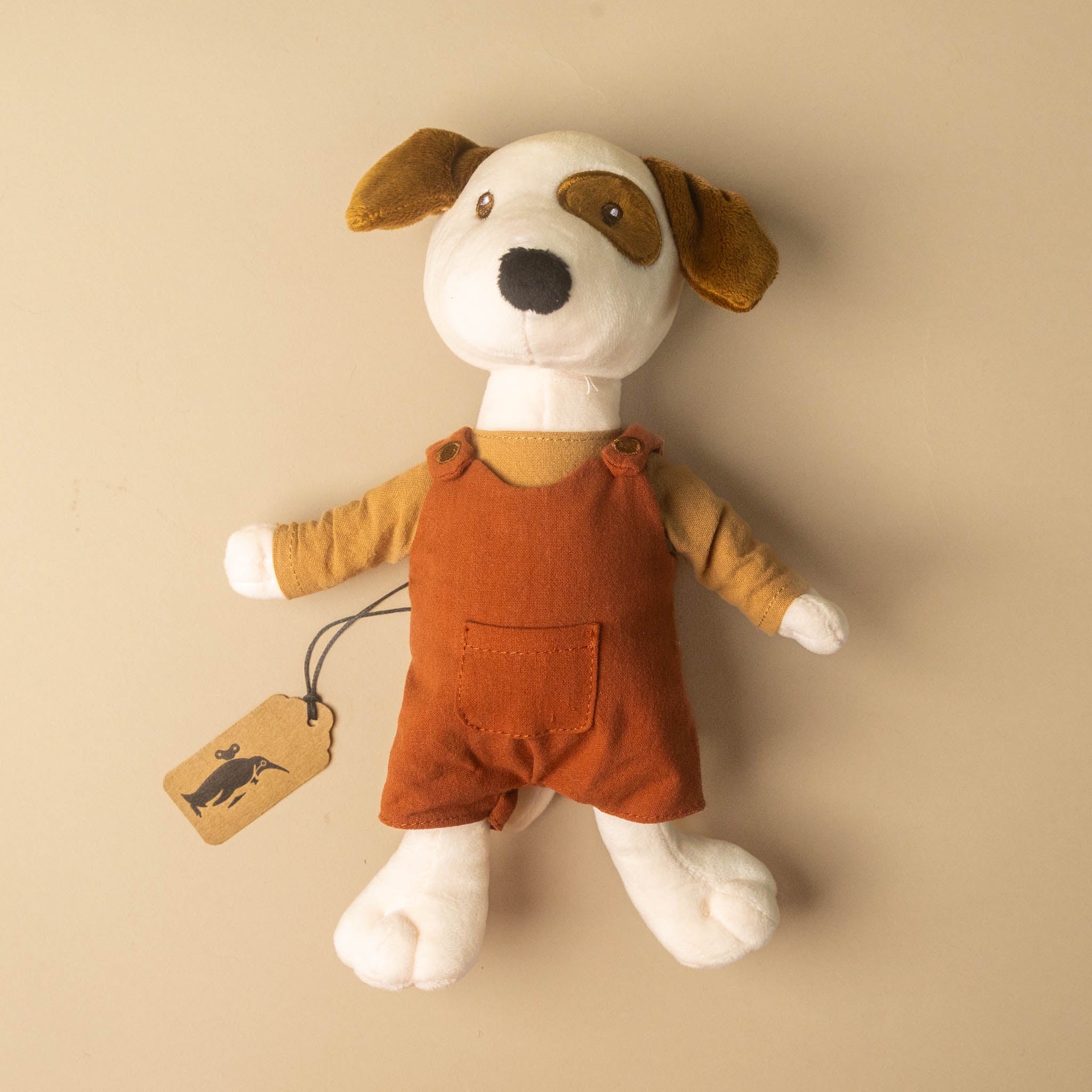 Stuffed eddie-the-pup toy with a brown outfit and tag on a beige background