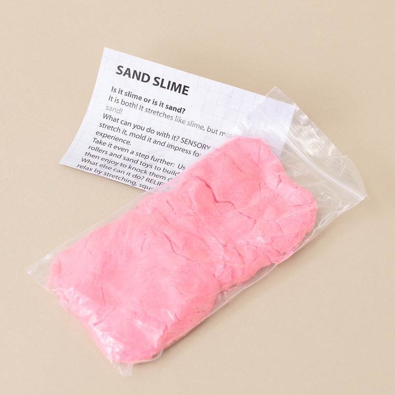 A clear plastic bag containing pink sand slime with an informational card labeled 'SAND SLIME' on a warm beige background.