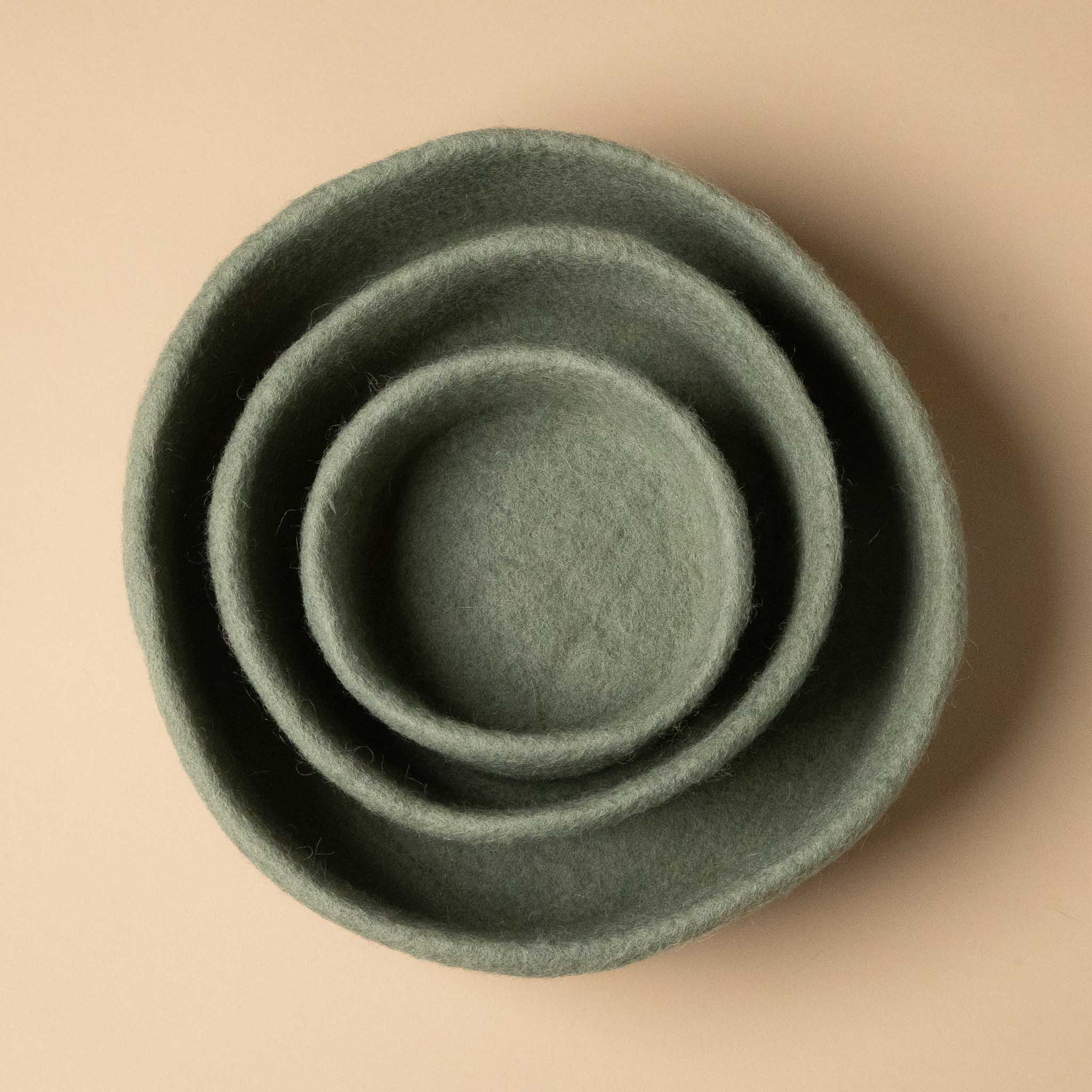 Set of three green felt bowls on a beige background