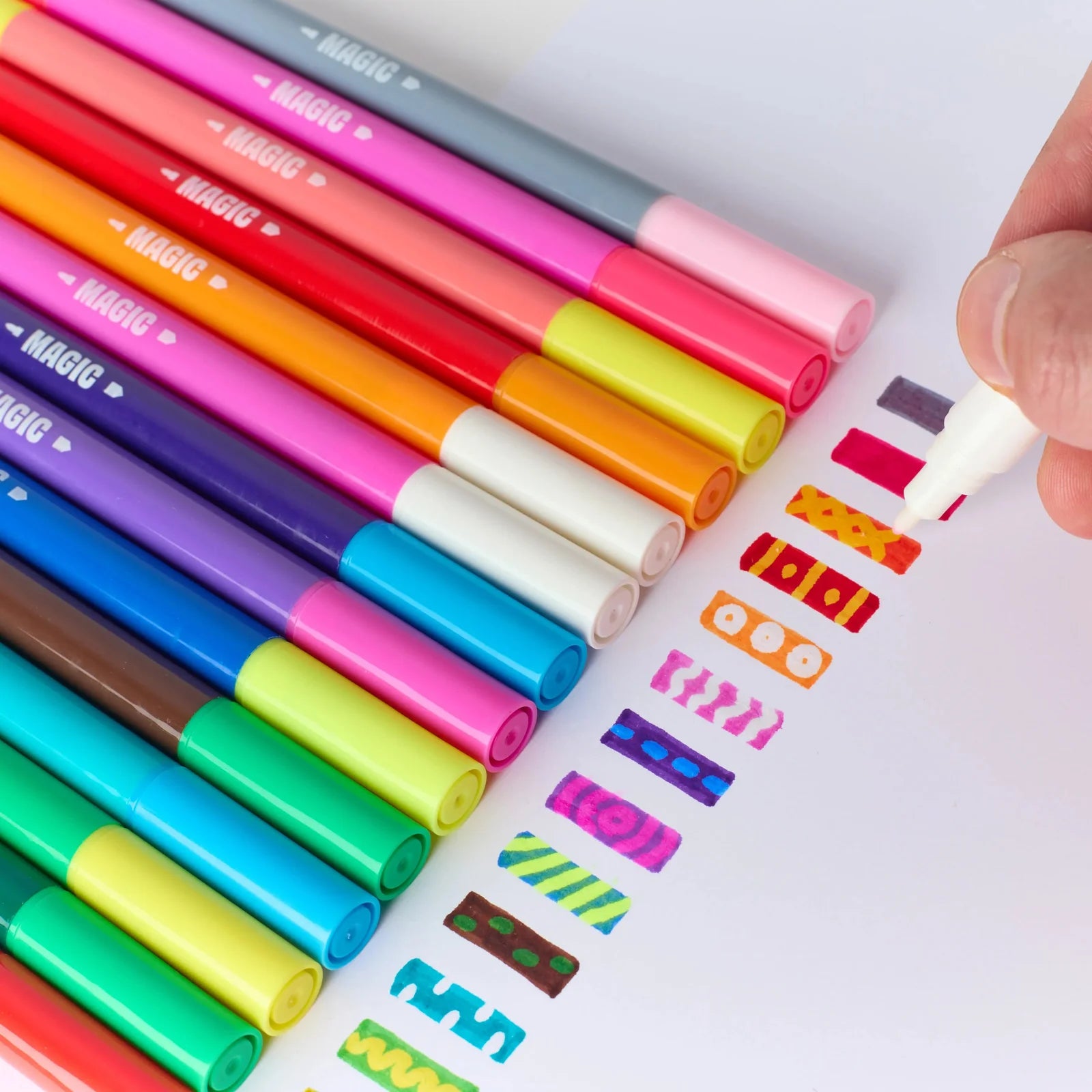 A close-up of a hand using a white-capped marker to draw colorful squiggly lines next to a fan of Magic brand markers in various colors on a white surface.