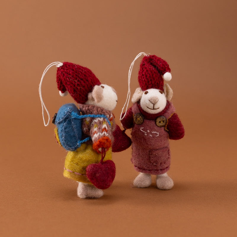 Two small felted wool ornaments mouse, standing on a warm brown background. One wears a red Santa hat, yellow dress, blue backpack, and red heart, while the other wears a red Santa hat and mauve overalls.