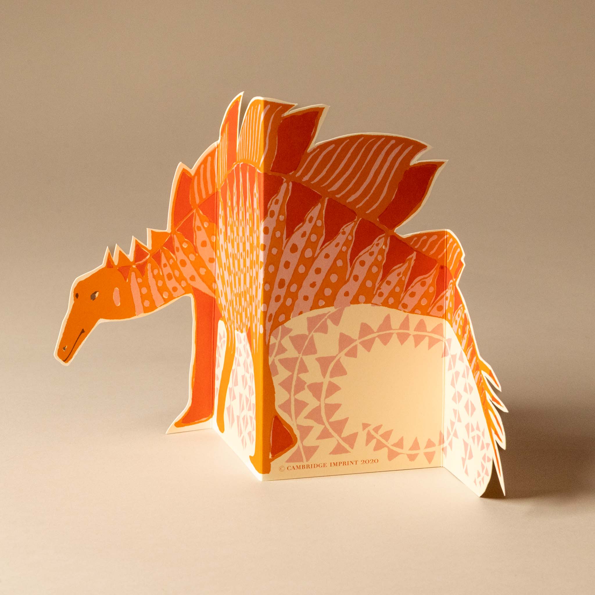 folding-stegosaurus-greeting-card--orange-3D paper model of a dinosaur with geometric patterns on a beige background
