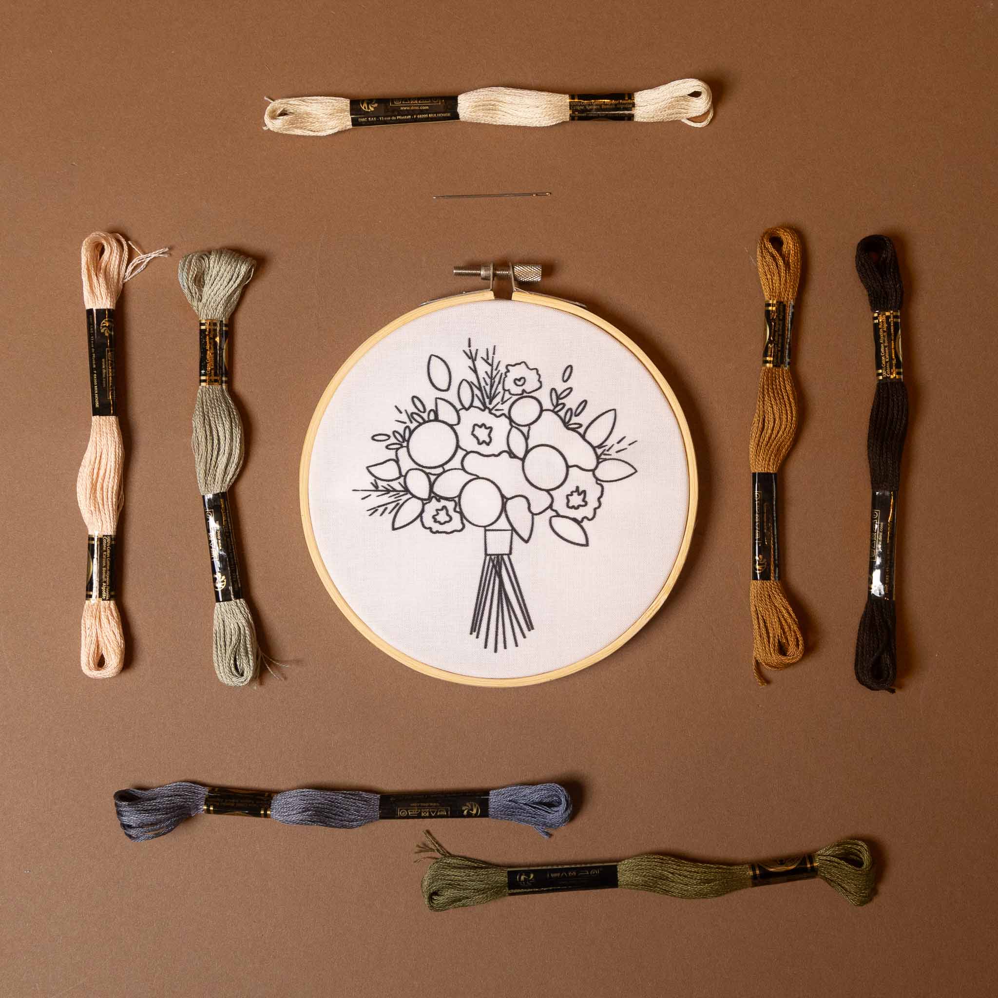 francesca-bouquet-embroidery-kit Embroidery hoop with floral design and assorted embroidery threads on a brown background
