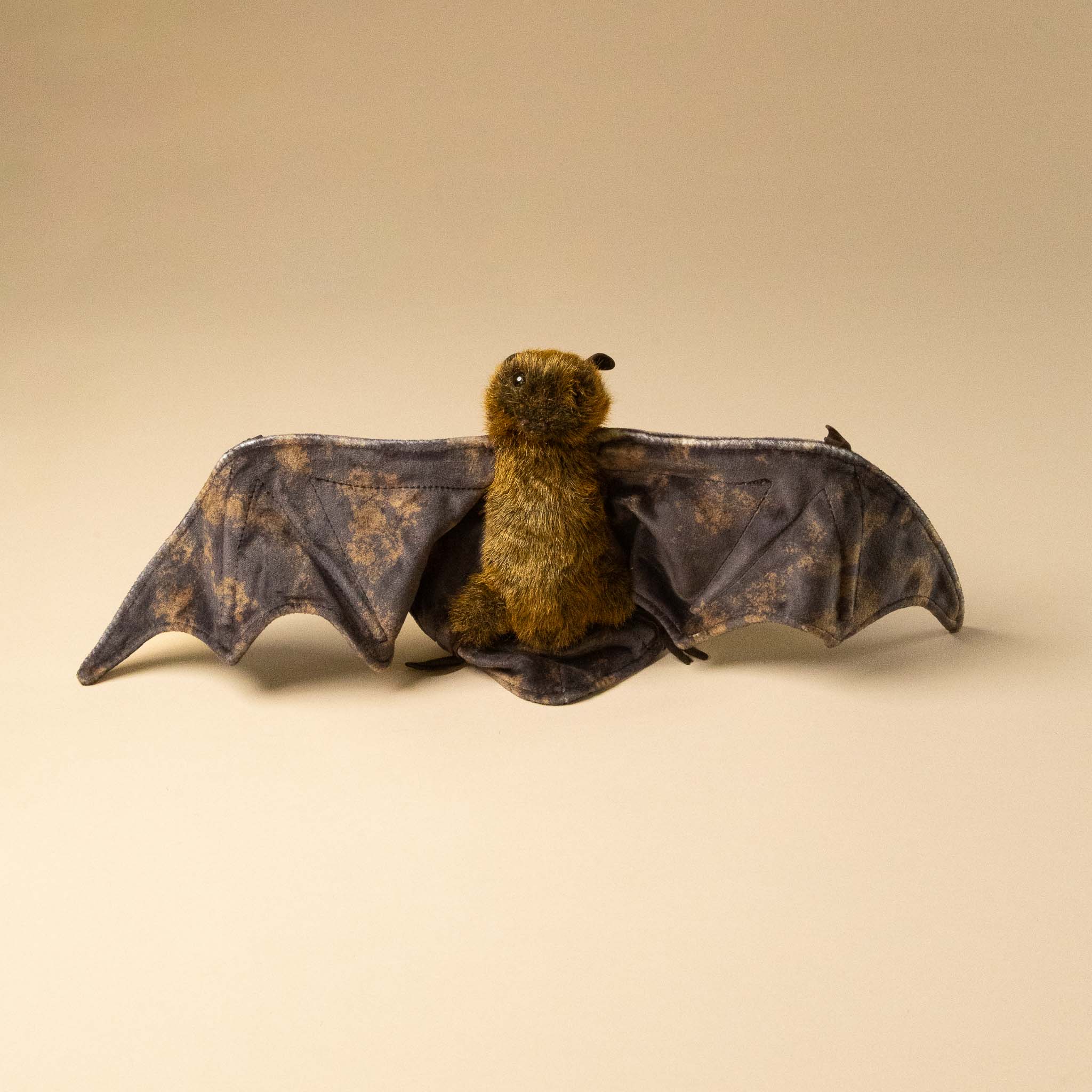 fruit-bat-hand-puppet toy with open wings on a beige background