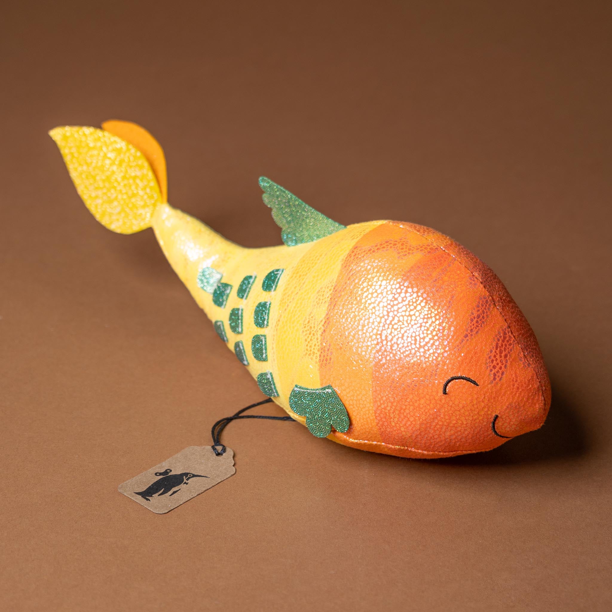 gil-the-guppie-fish Plush toy resembling a fish with a tag on a brown background