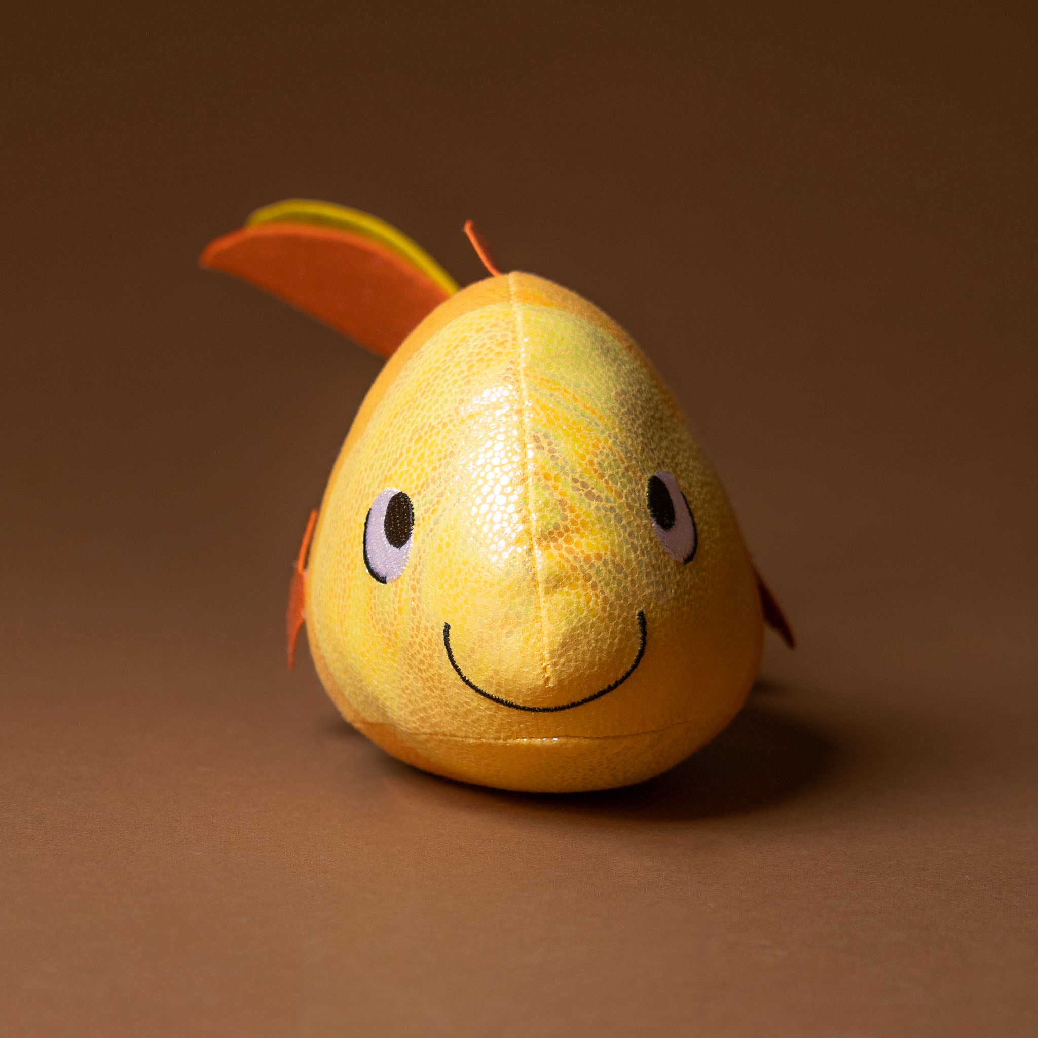 gus-the-guppie-fish Plush toy shaped like a pear with a face on a brown background