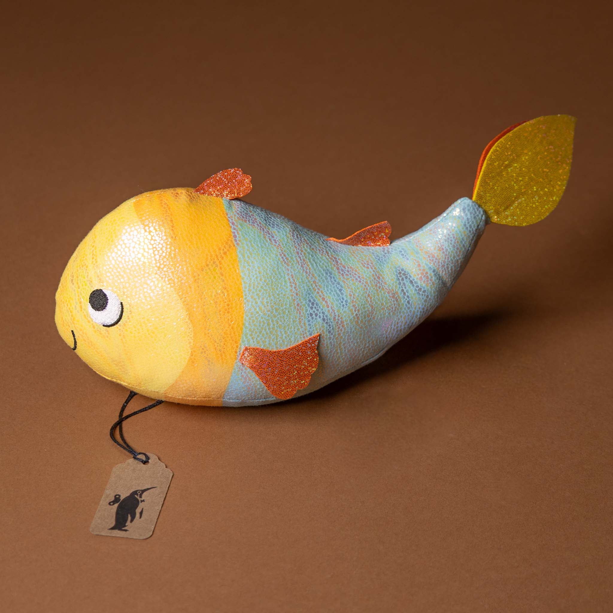 gus-the-guppie-fish Colorful fish-shaped toy with a tag on a brown background