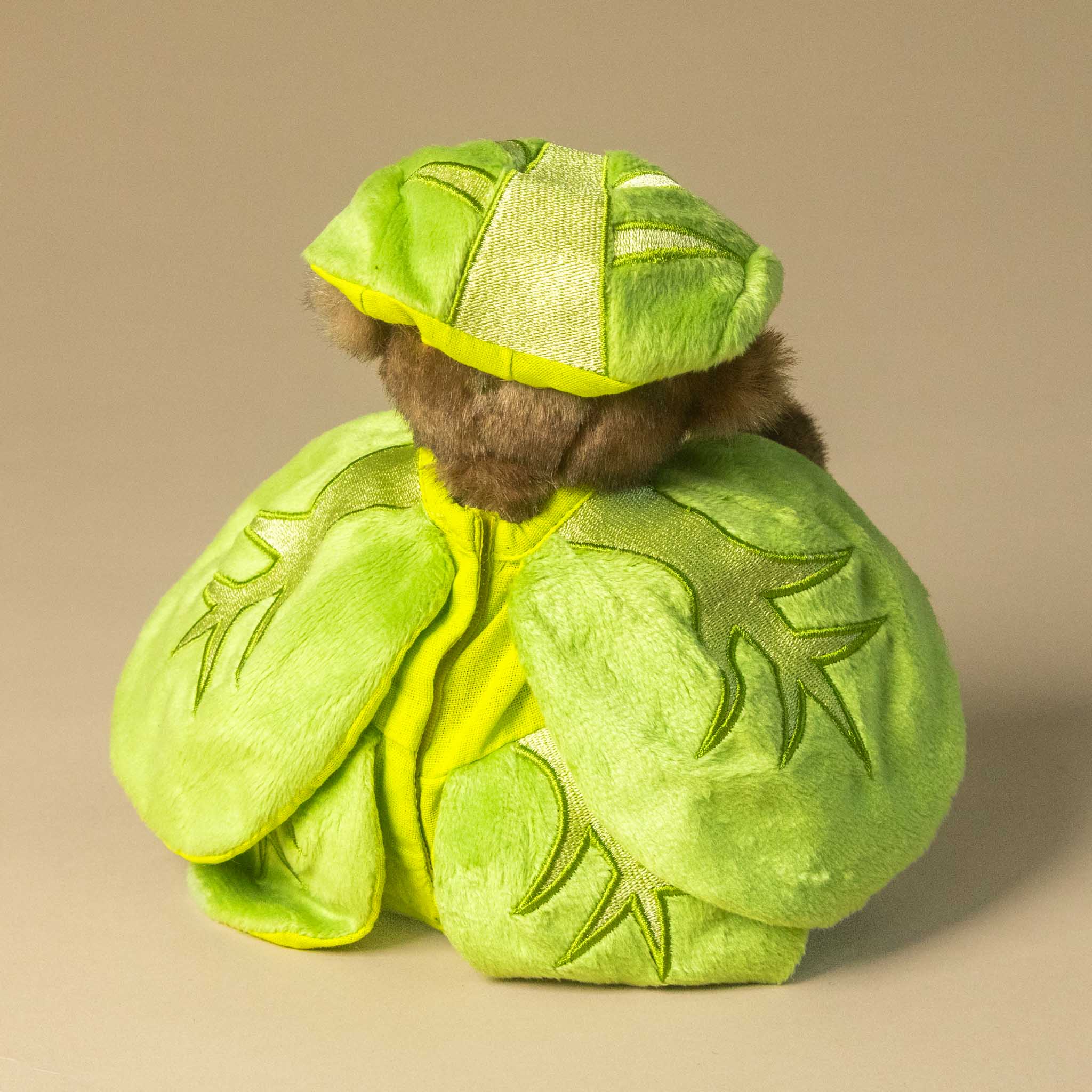 gustus-bear-the-brussel-sprout wearing a green leaf costume on a beige background