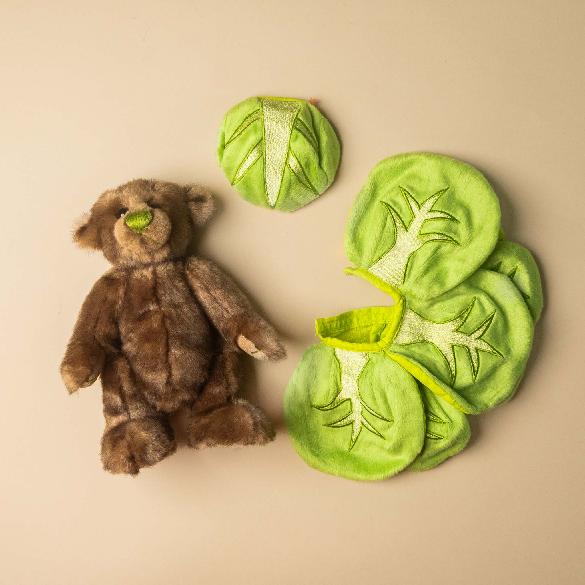 gustus-bear-the-brussel-sprout next to green Brussels sprout-shaped toys on a beige background