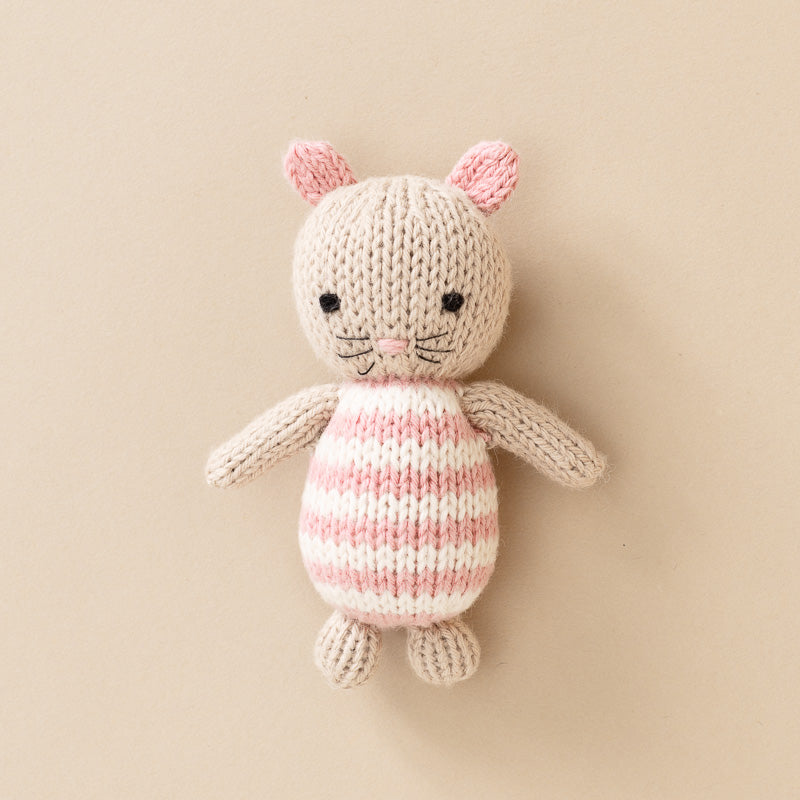 A hand-knit-pocket-mouse toy with a cream-colored body, pink and cream horizontal stripes on its belly and ears, and black embroidered eyes and whiskers, set against a solid beige background.