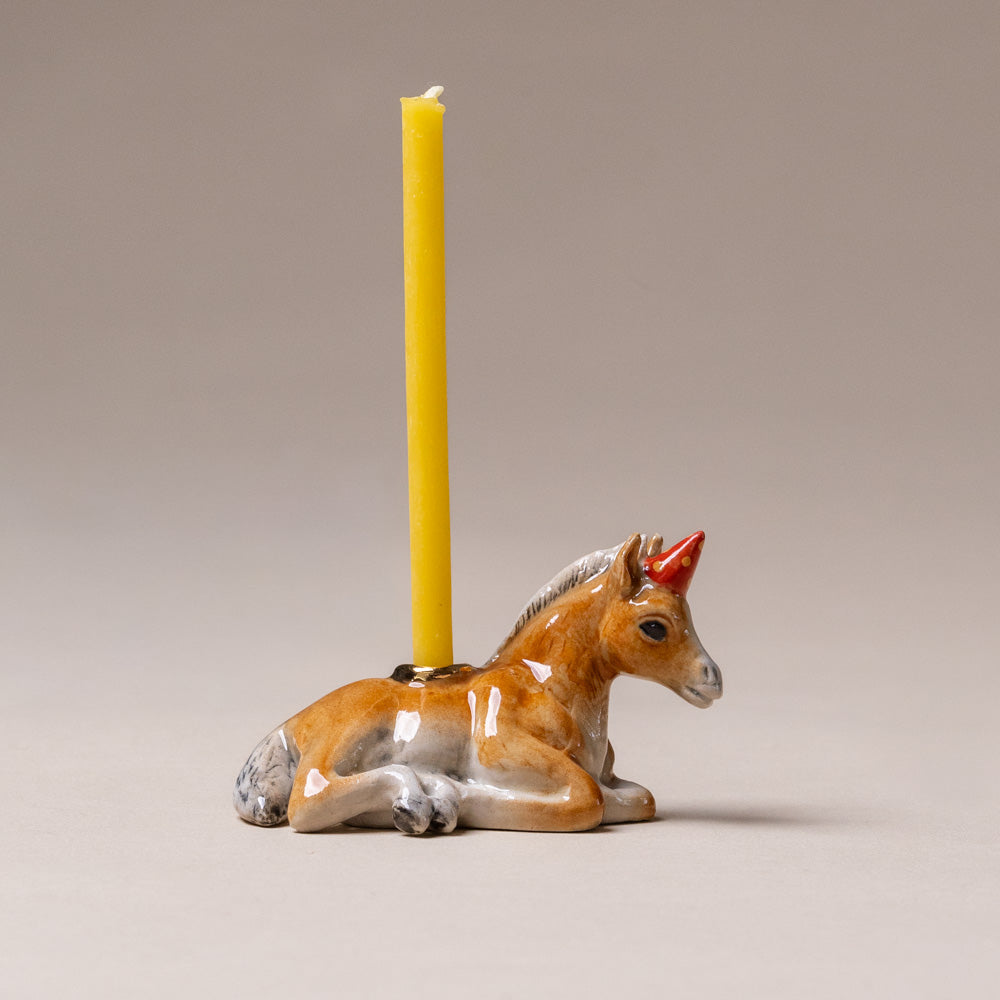 heirloom-porcelain-cake-topper-horse Ceramic horse-shaped candle holder with a lit yellow candle on a neutral background