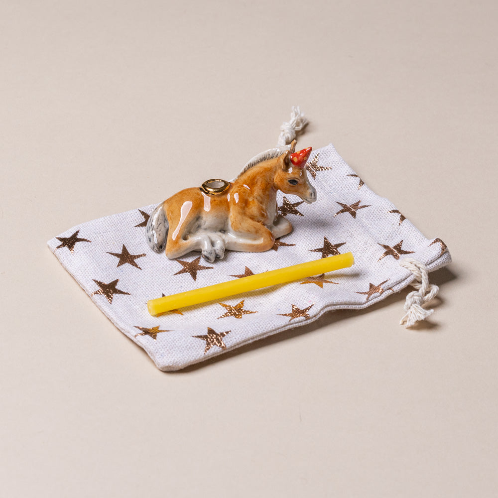 heirloom-porcelain-cake-topper-horse Small ceramic deer figurine with a yellow candle on a star-patterned cloth against a beige background