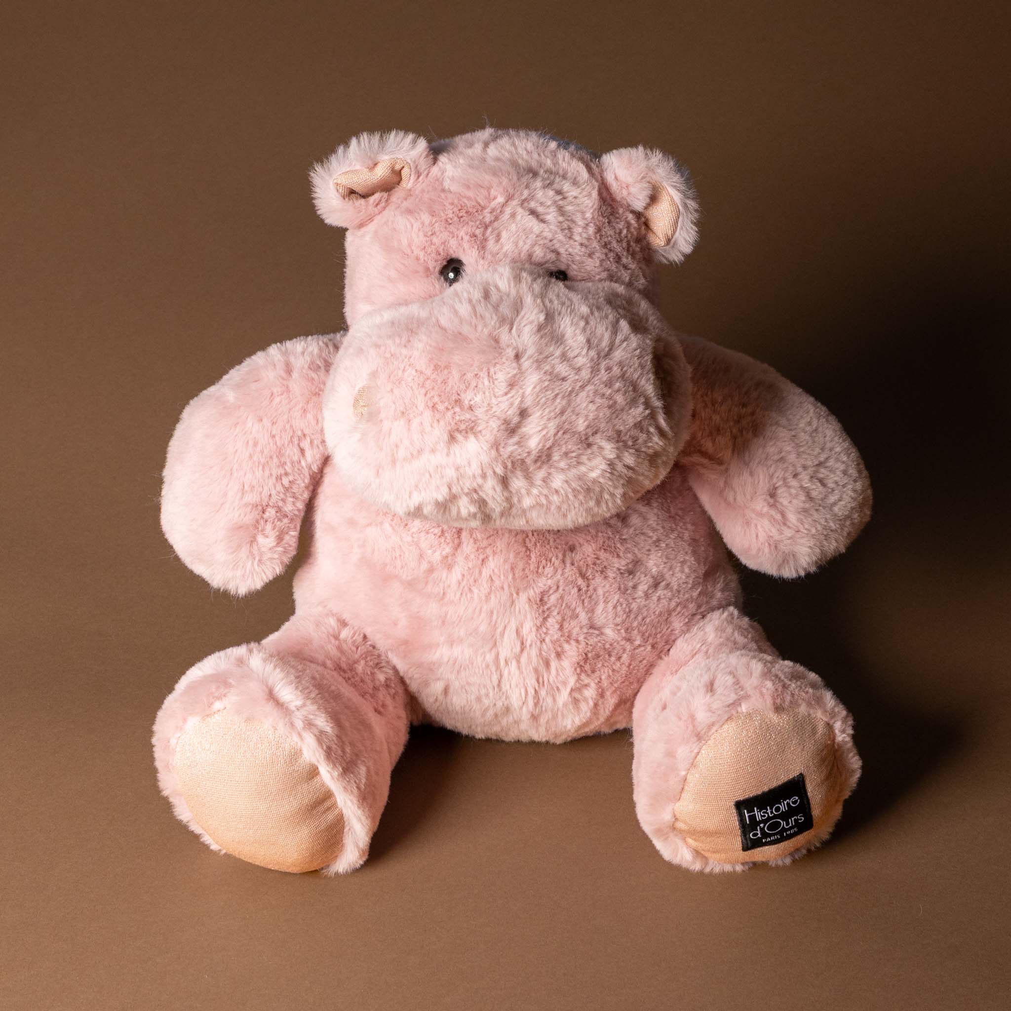hip-hippo-blush-medium Pink plush hippo toy with a visible brand label on a brown background
