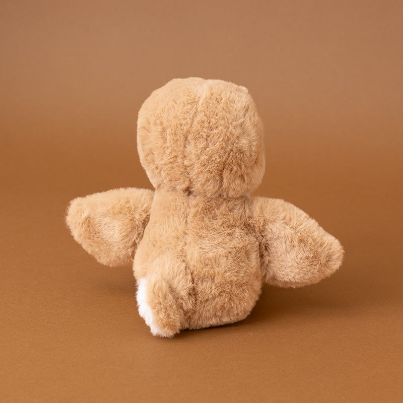 A light brown plush teddy bear toy shown from the back, featuring soft textured fur and a small white patch on its back feet, set against a solid warm brown background.