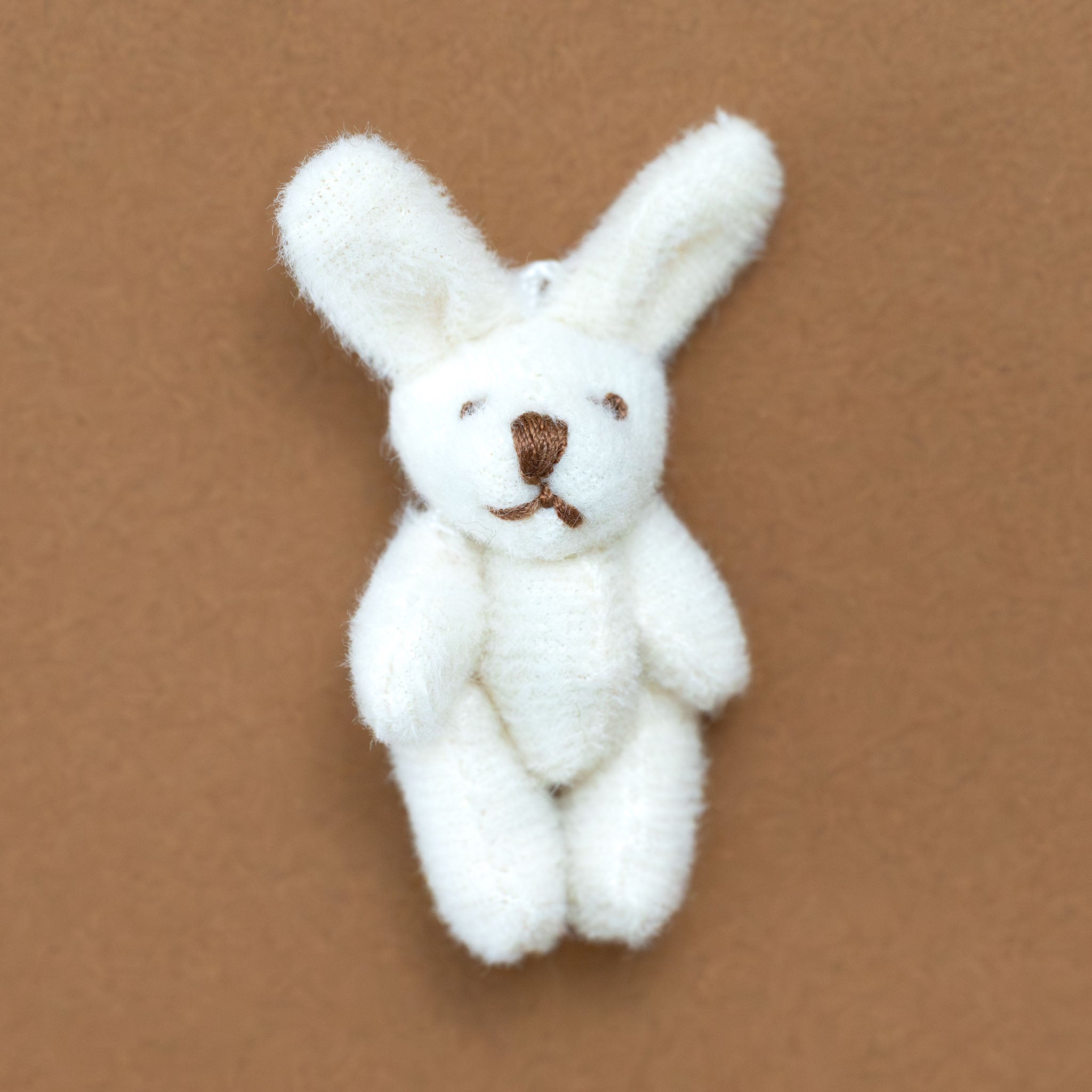 itty-bitty-bunny--coconut Small white stuffed bunny toy on a brown background