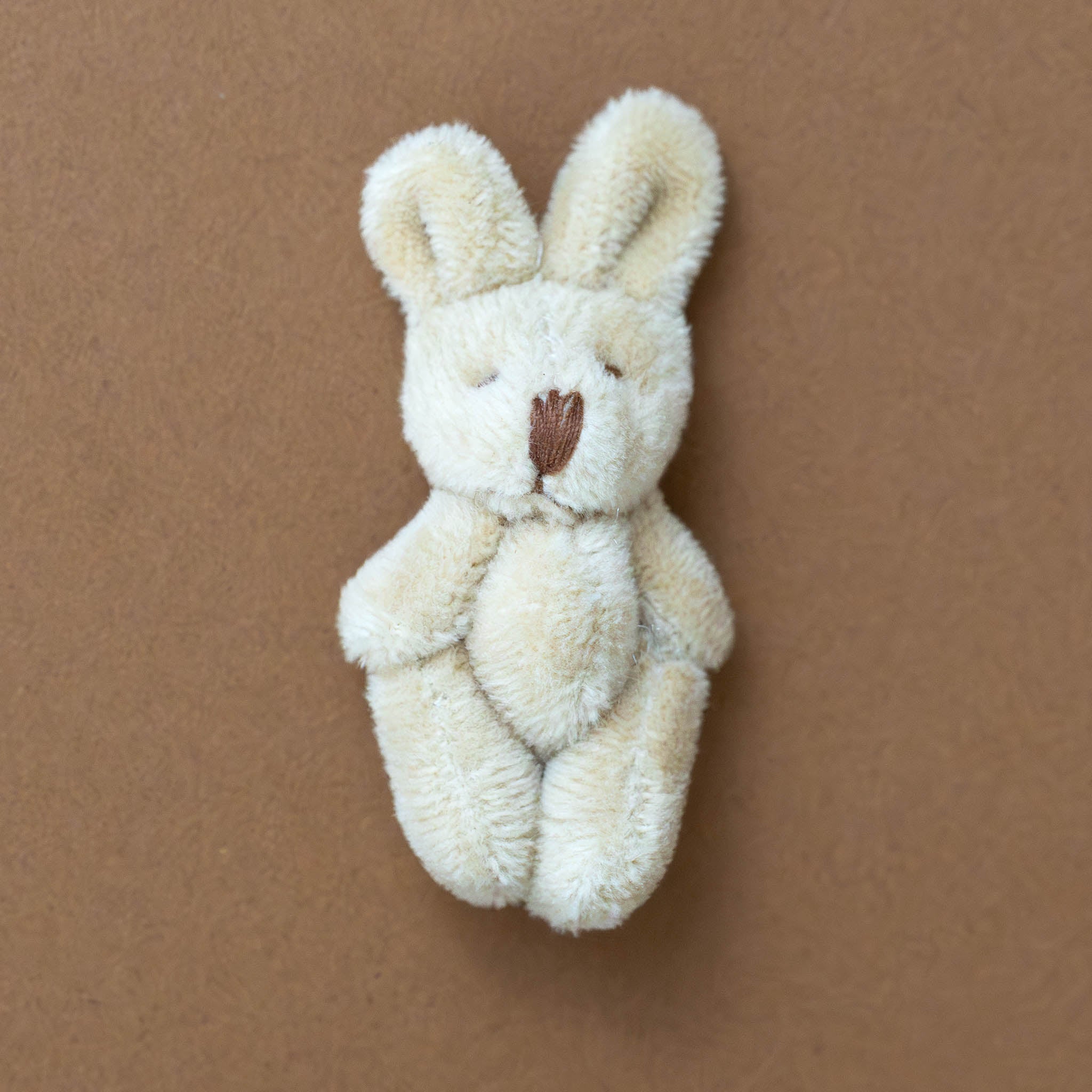 itty-bitty-bunny-oatmeal Small cream-colored plush bunny toy on a brown background