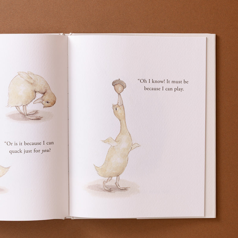 An open children's book spread showing watercolor-style illustrations of a duckling balancing acorns on its head and text on warm off-white pages, photographed against a brown background.