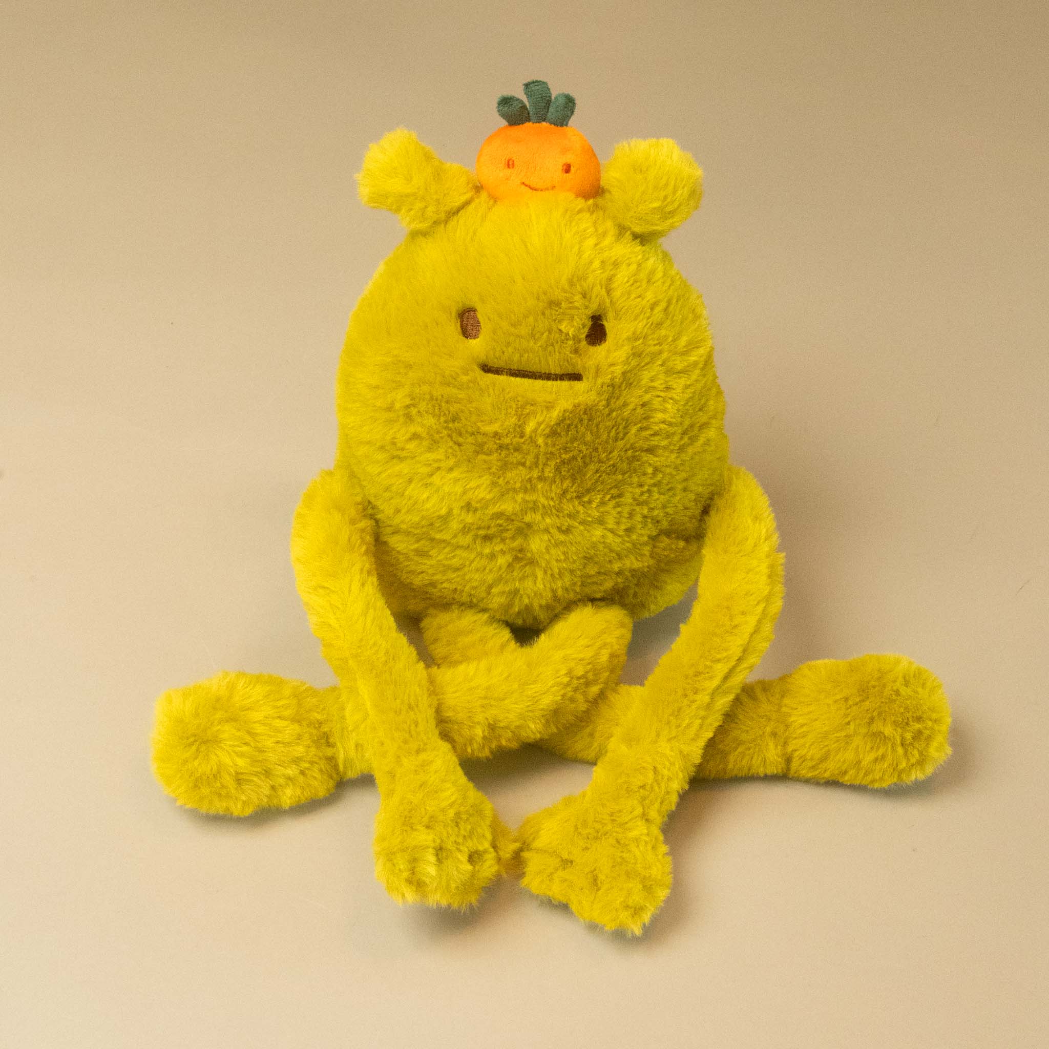 A yellow laurent-jade-petit plush toy with long limbs, a stitched face, and a small jade fruit character on its head, photographed against a plain light beige background.