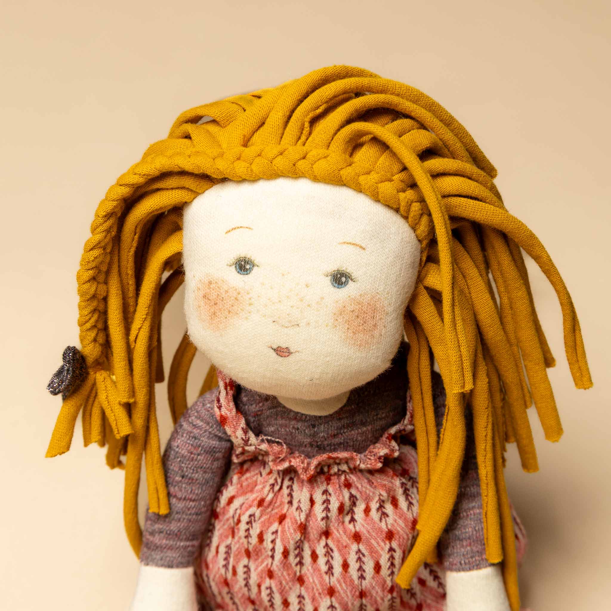 les-rosalie-rag-doll-vanille Textile doll with yellow hair and a patterned dress on a beige background