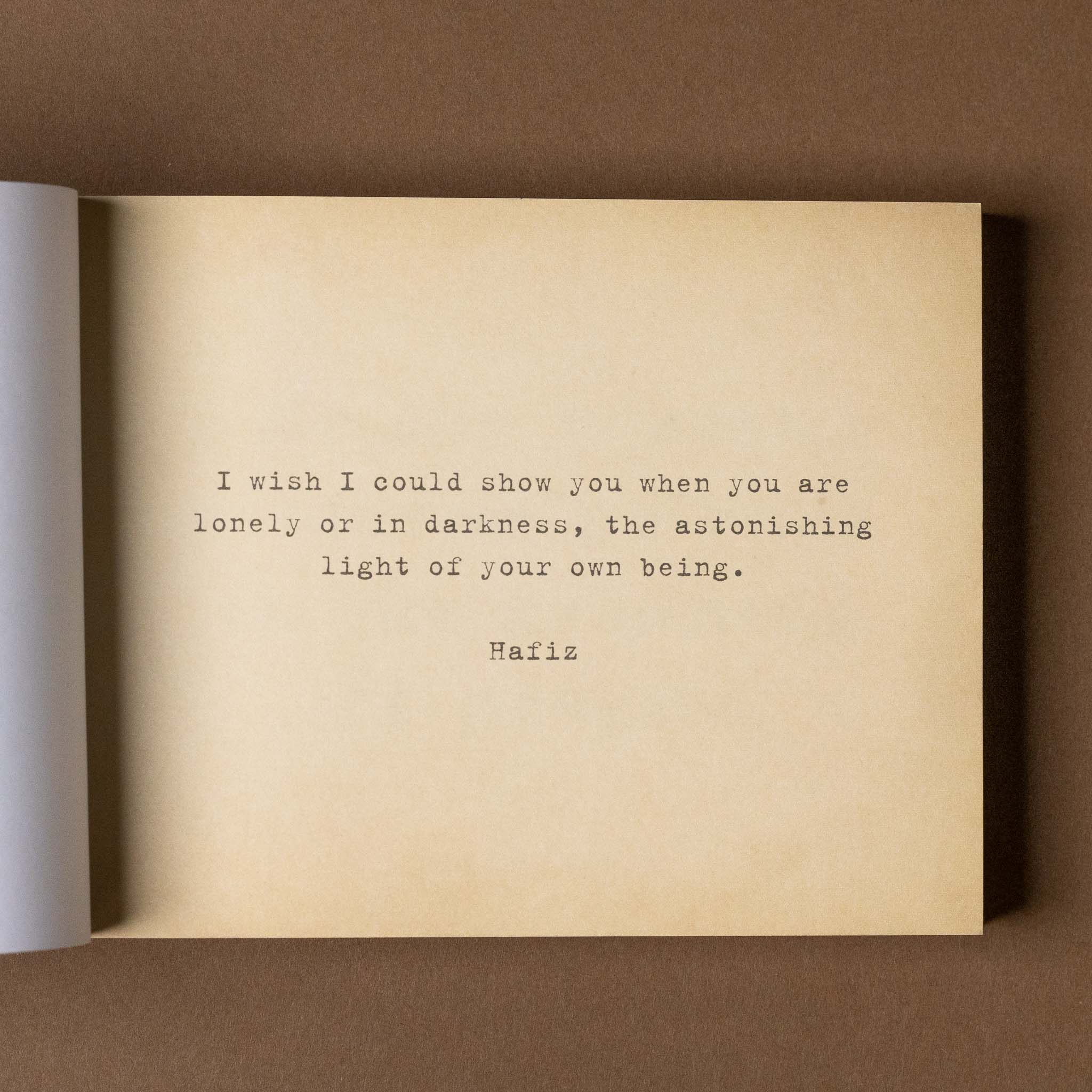 Open book with a Hafiz quote on a brown background