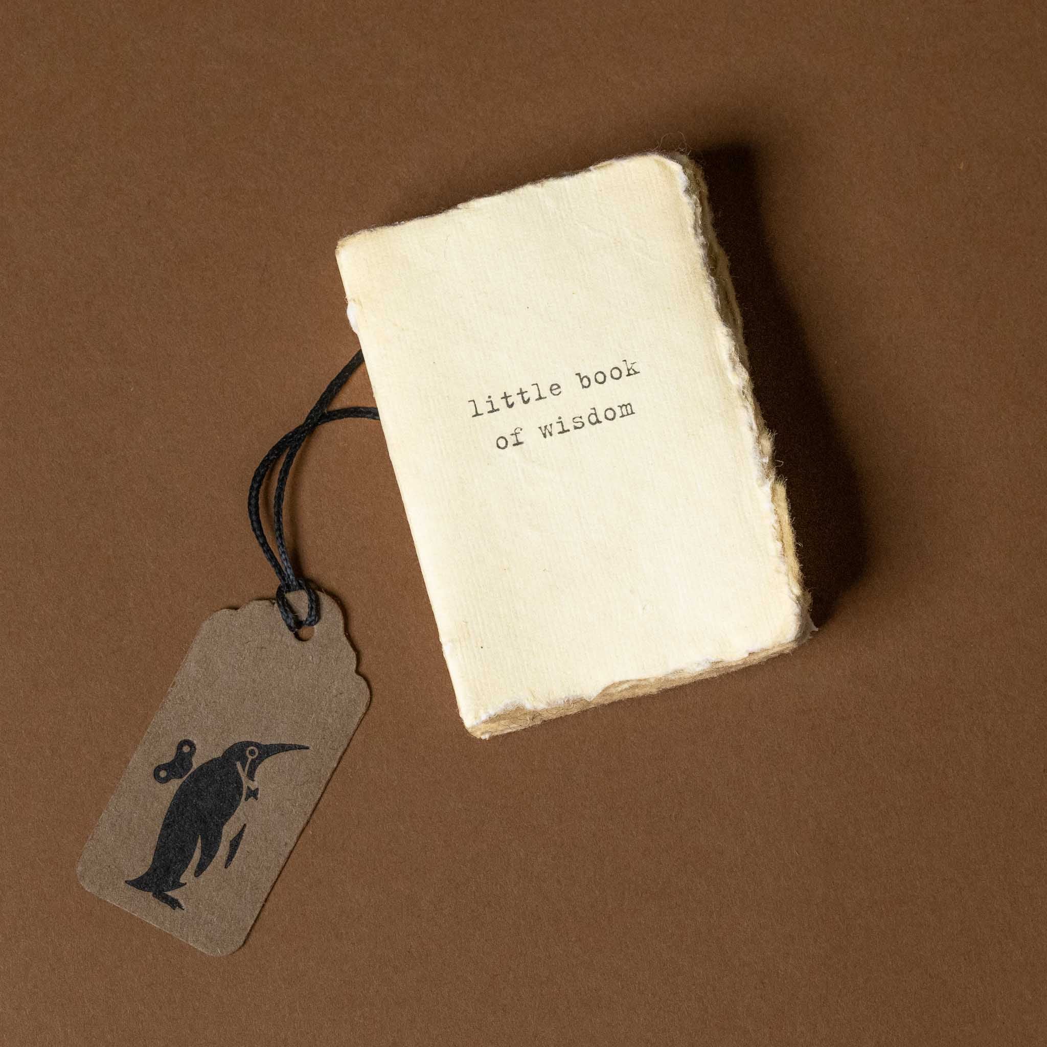 Small book titled 'little book of wisdom' with a tag on a brown background